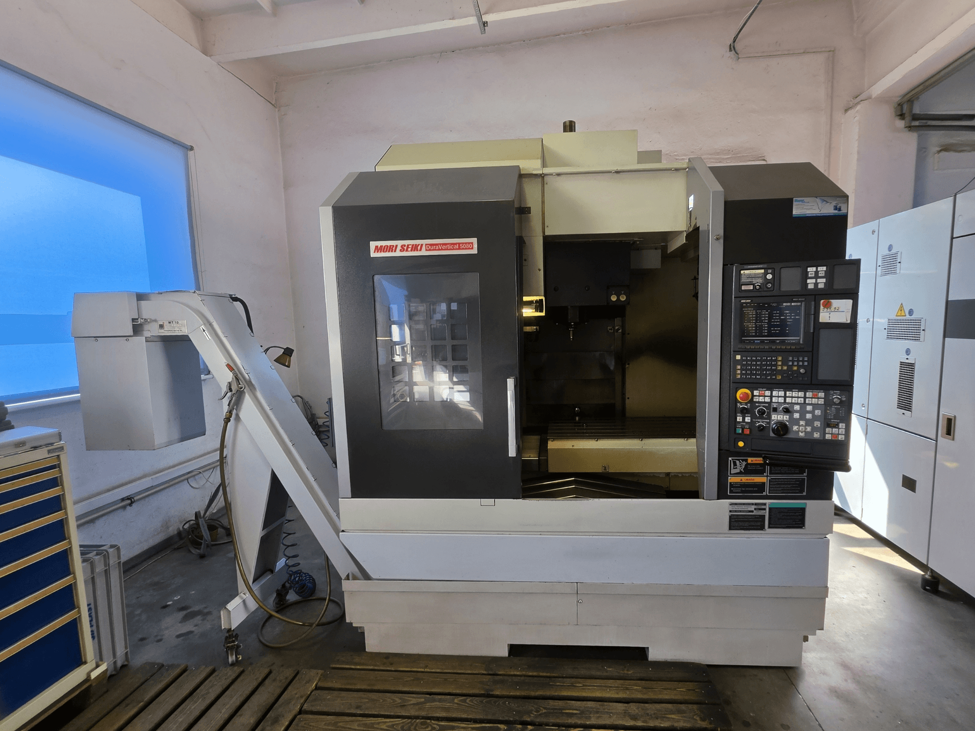 Vertikalusis apdirbimo centras „MORI SEIKI DuraVertical 5080“, vaizdas iš priekio, kuriame matomas valdymo skydas, suklis ir įrankių laikiklis.