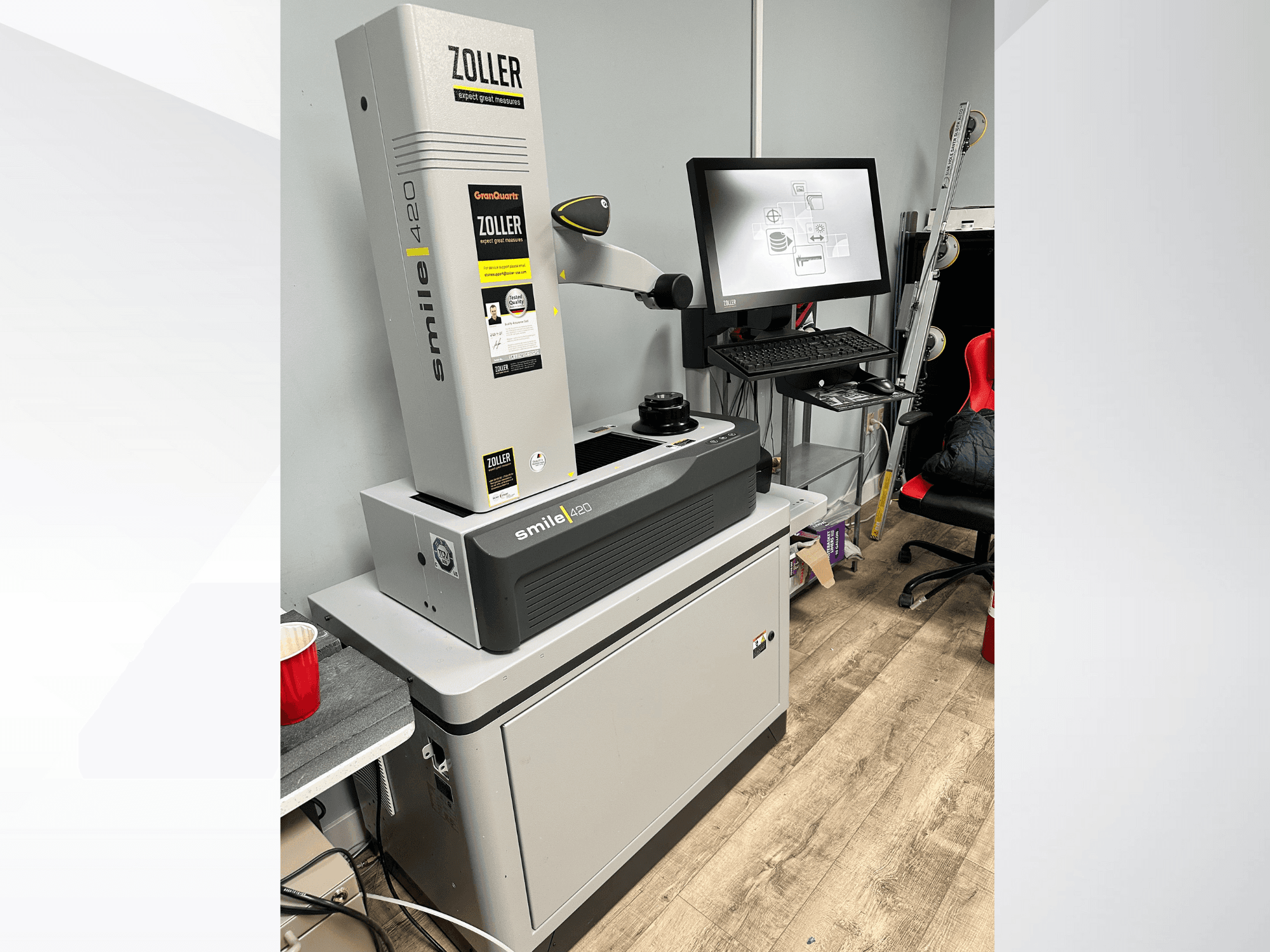 Skaitmeninė matavimo mašina "Zoller Smile 420", parodyta iš priekio, o fone - monitorius ir darbo vieta.