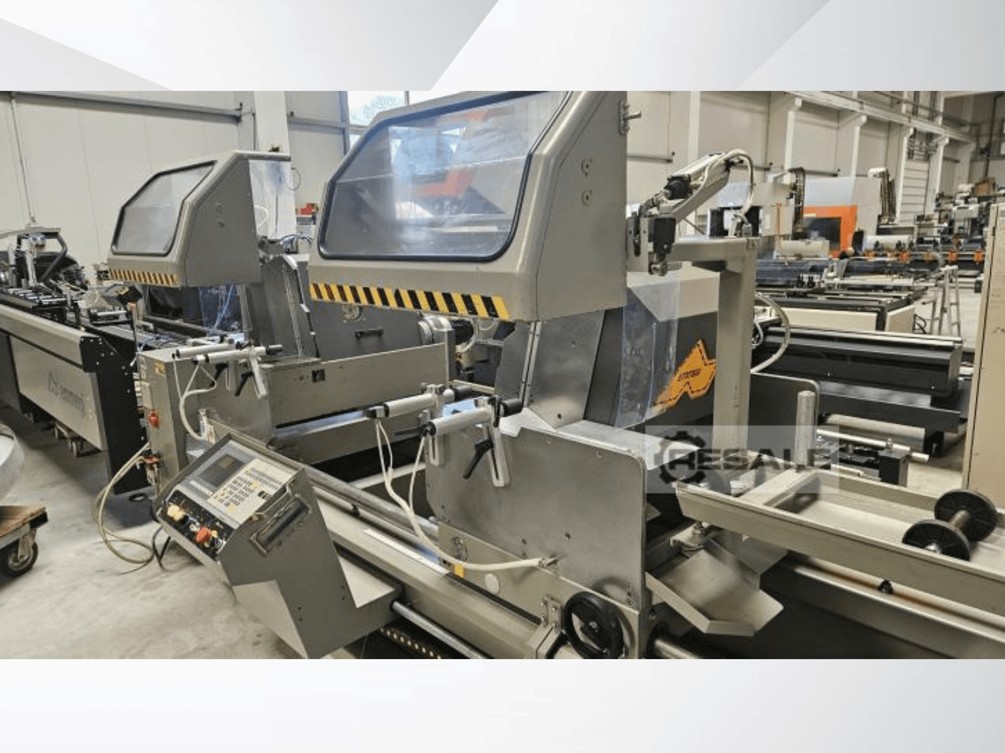 Dvigubo pjovimo staklės gamykloje; priekinis vaizdas, kuriame matyti valdymo skydelis, stiklo dangteliai ir pjovimo komponentai.