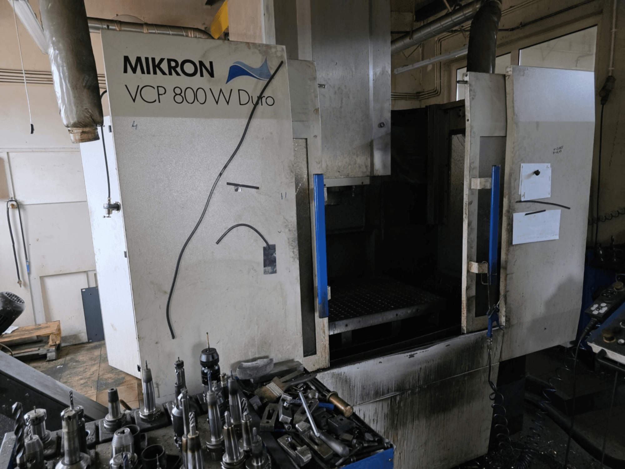 Mikron VCP 800 W Duro frezavimo staklės, parodytos iš šono, pirmame plane matomi įrankiai ir valdikliai.