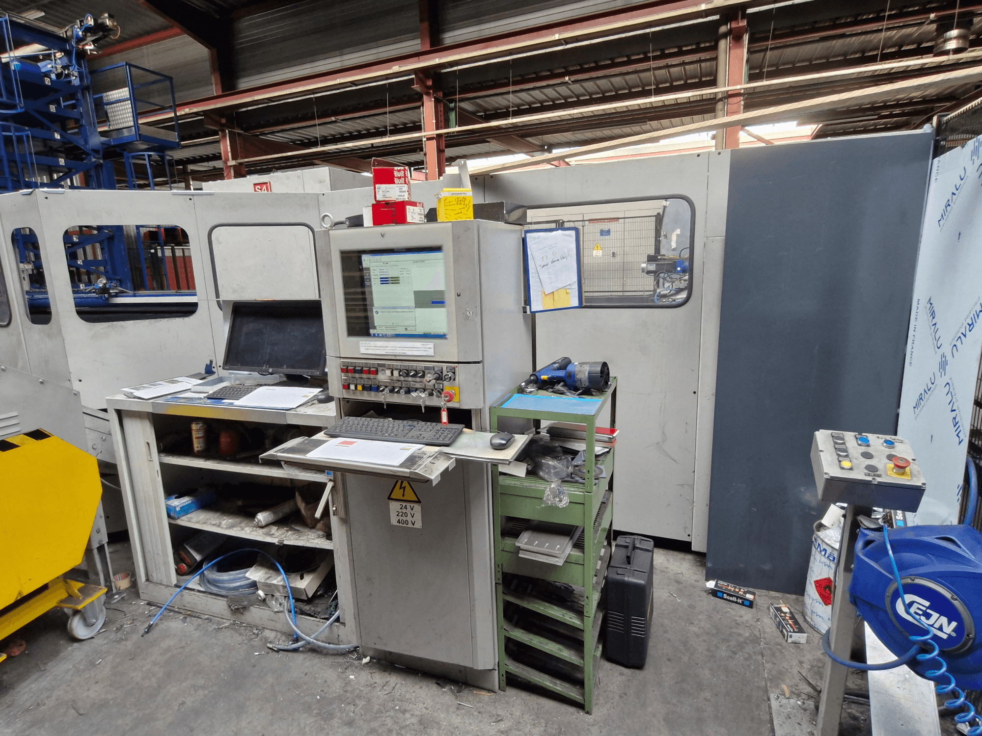CNC perforavimo staklės "Salvagnini S4-40" dirbtuvėse, su valdymo pultu, monitoriais ir įrankiais, vaizdas iš priekio.