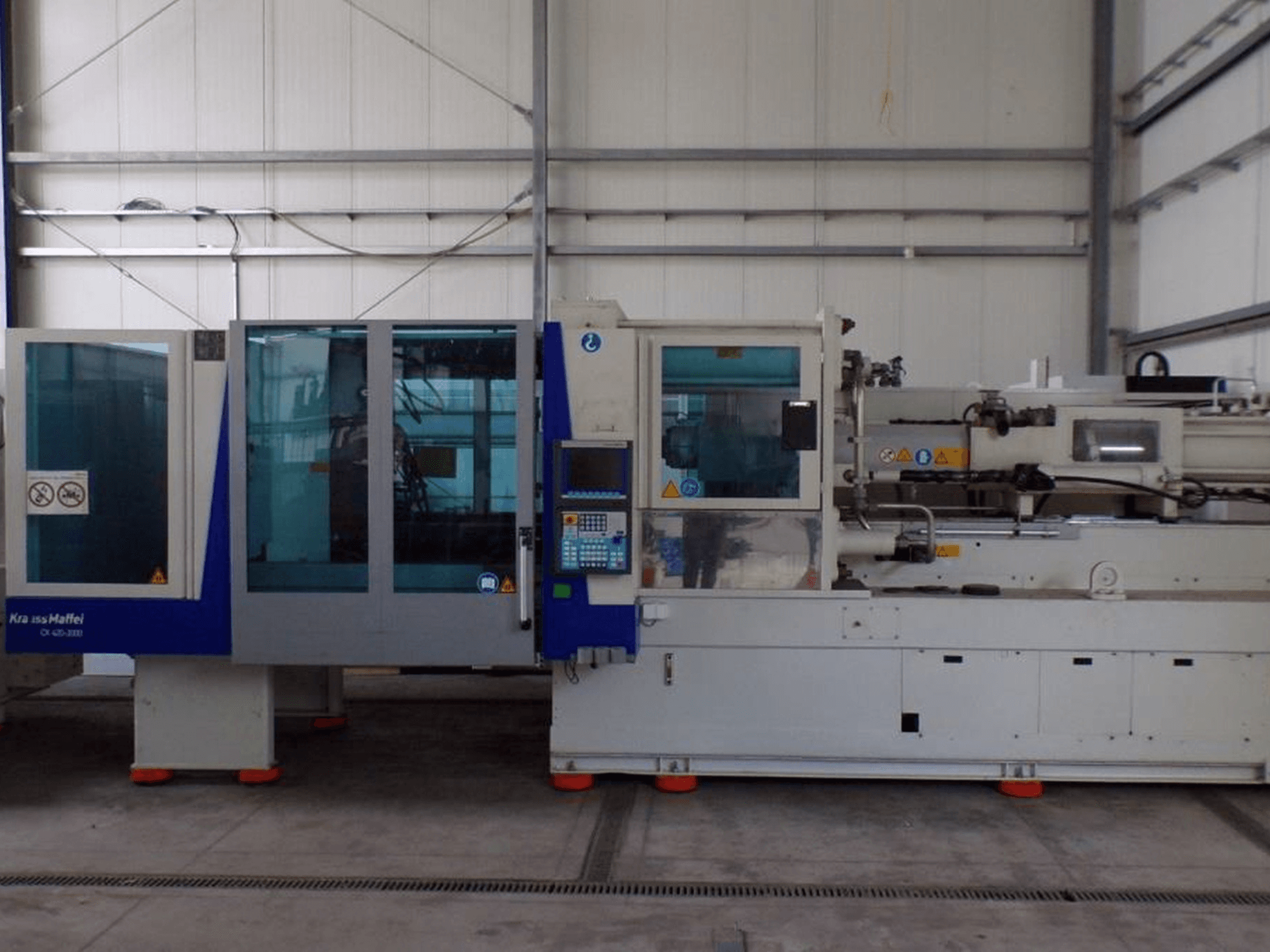"KraussMaffei" įpurškimo liejimo mašina, vaizdas iš šono, valdymo skydelis ir saugos indikatoriai, matomi gamykloje.