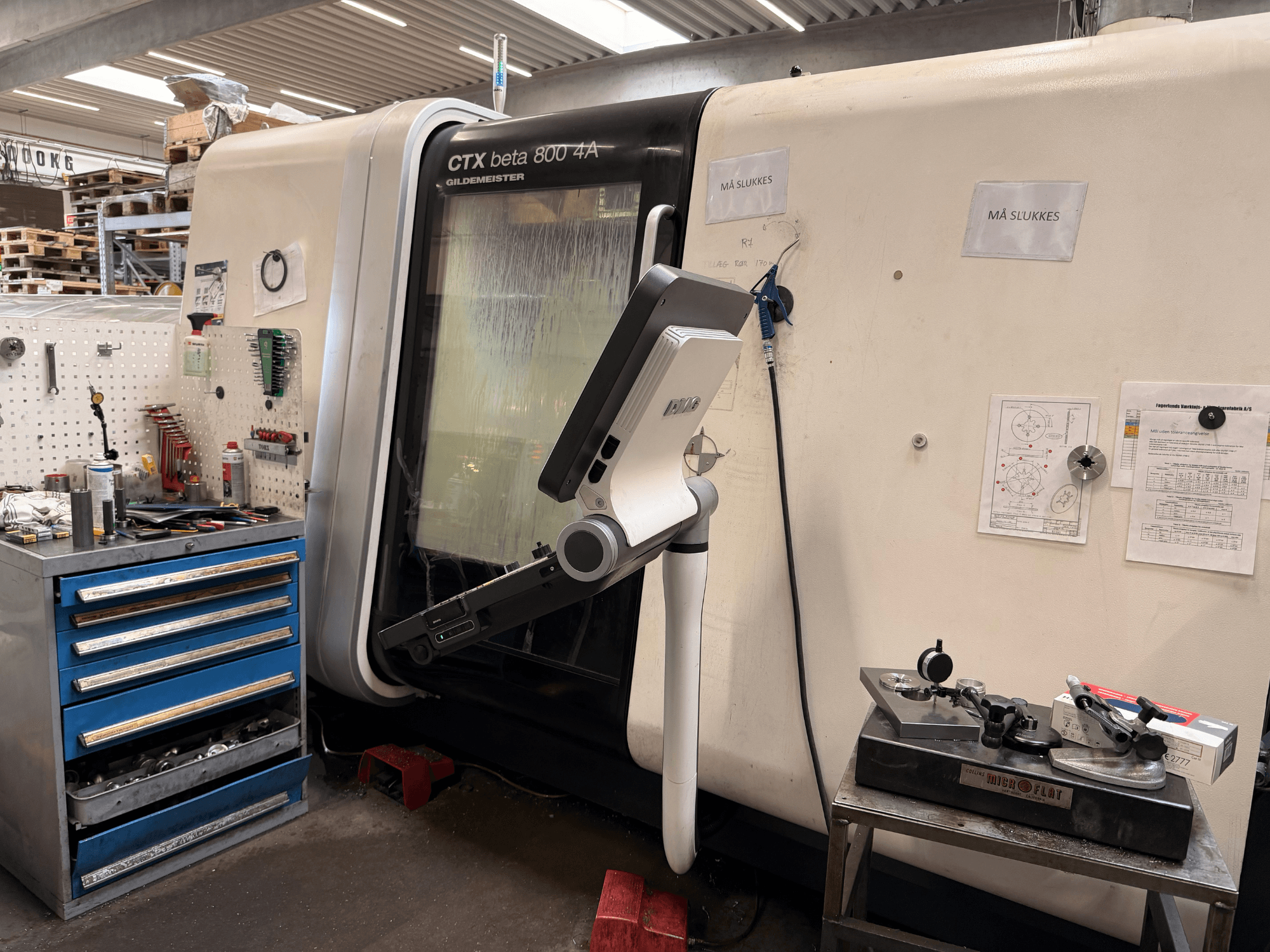DMG MORI CTX Beta 800 4a vertikaliojo tekinimo staklės dirbtuvėse su valdymo svirtimi ir šalia esančiais techniniais dokumentais.