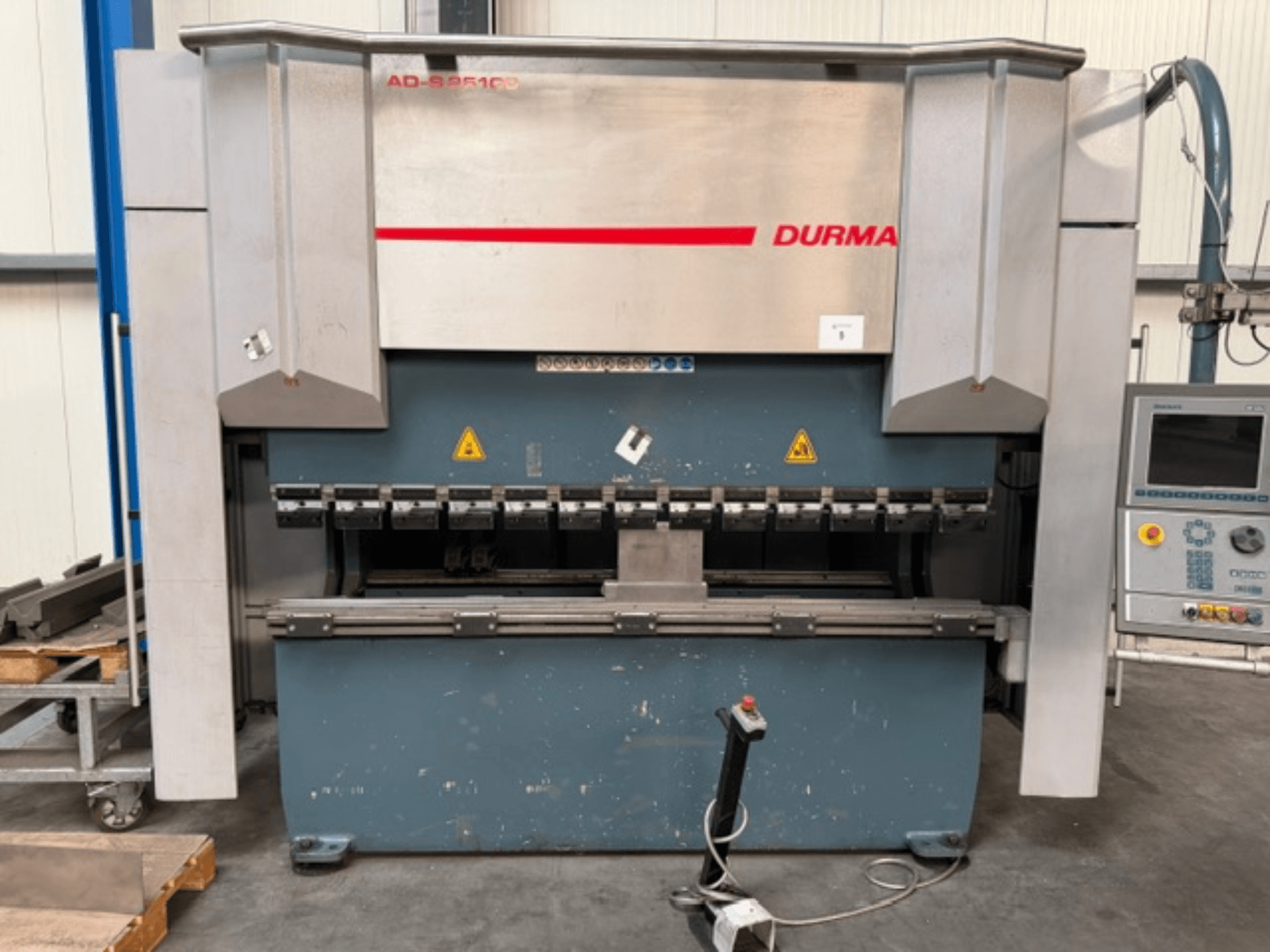 „Durma ADS 25100“ lenkimo presas, vaizdas iš priekio su valdymo pultu, kuriame matomi lenkimo įrankiai ir saugos etiketės.