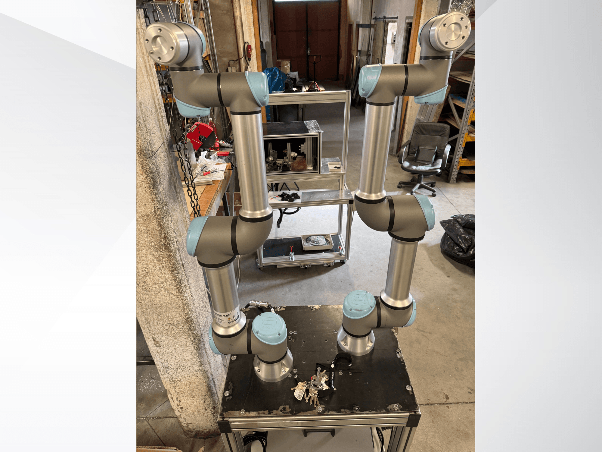 „Universal Robots“ UR5e robotinė ranka, pavaizduota iš viršaus, kurioje matoma daugiasąnarė aliuminio konstrukcija ir pilkai mėlynos spalvos sąnariai.
