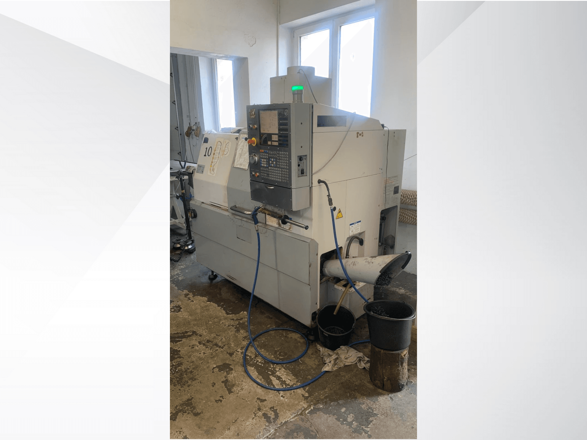 "Haas" CNC staklių modelis su valdymo skydeliu, vaizdas iš šono, su aušinimo skysčio linija, atliekų lataku ir apačioje esančiais laikymo konteineriais.