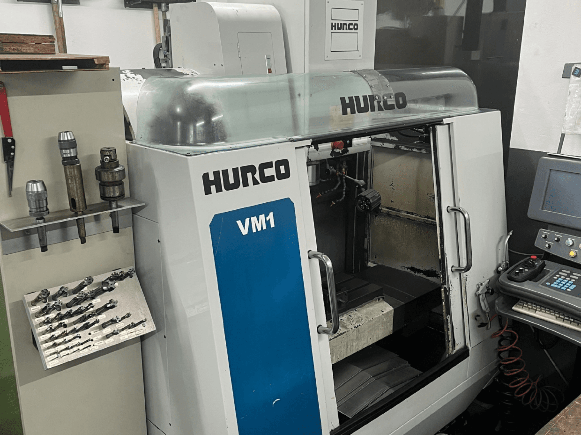 Vertikalaus apdirbimo centro "Hurco VM1" vaizdas iš priekio: permatomas dangtis, valdymo skydelis ir sumontuoti įrankiai.