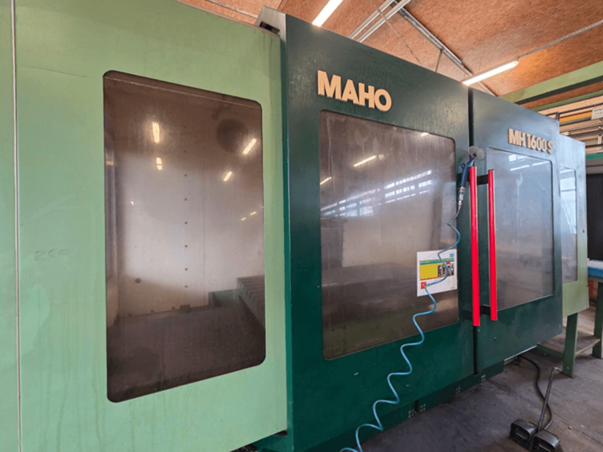Universalaus apdirbimo centro "MAHO 1600S" su dviem permatomomis plokštėmis ir valdymo pultu su raudonomis rankenėlėmis vaizdas iš priekio.