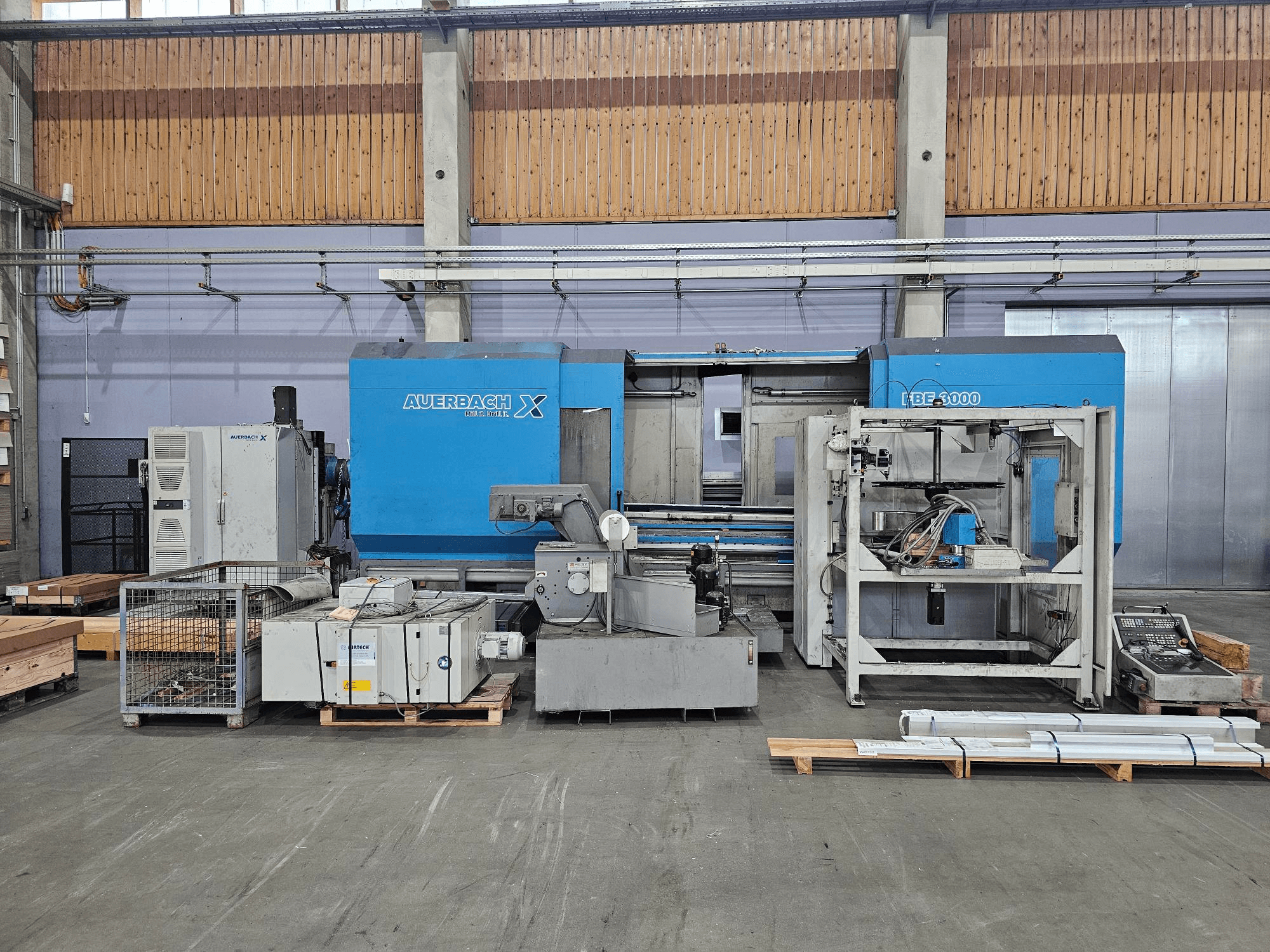 Auerbach X LBF-3000 mašina gamykloje, vaizdas iš šono, pilkos ir mėlynos spalvos komponentai su matomu valdymo skydeliu.