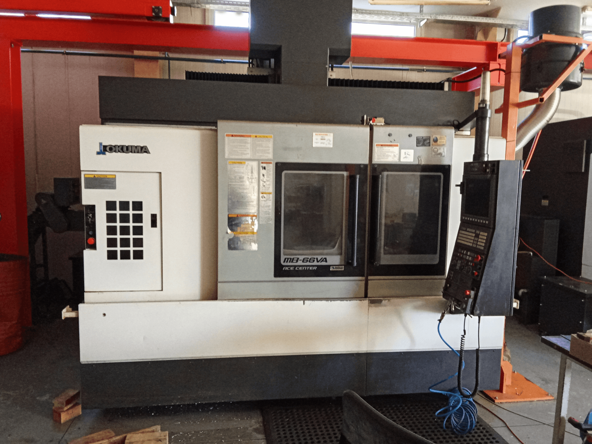 "Okuma MB-66VA" vertikalusis apdirbimo centras, priekinis vaizdas, kuriame matomas valdymo skydelis ir du langai įrankių prieigai.