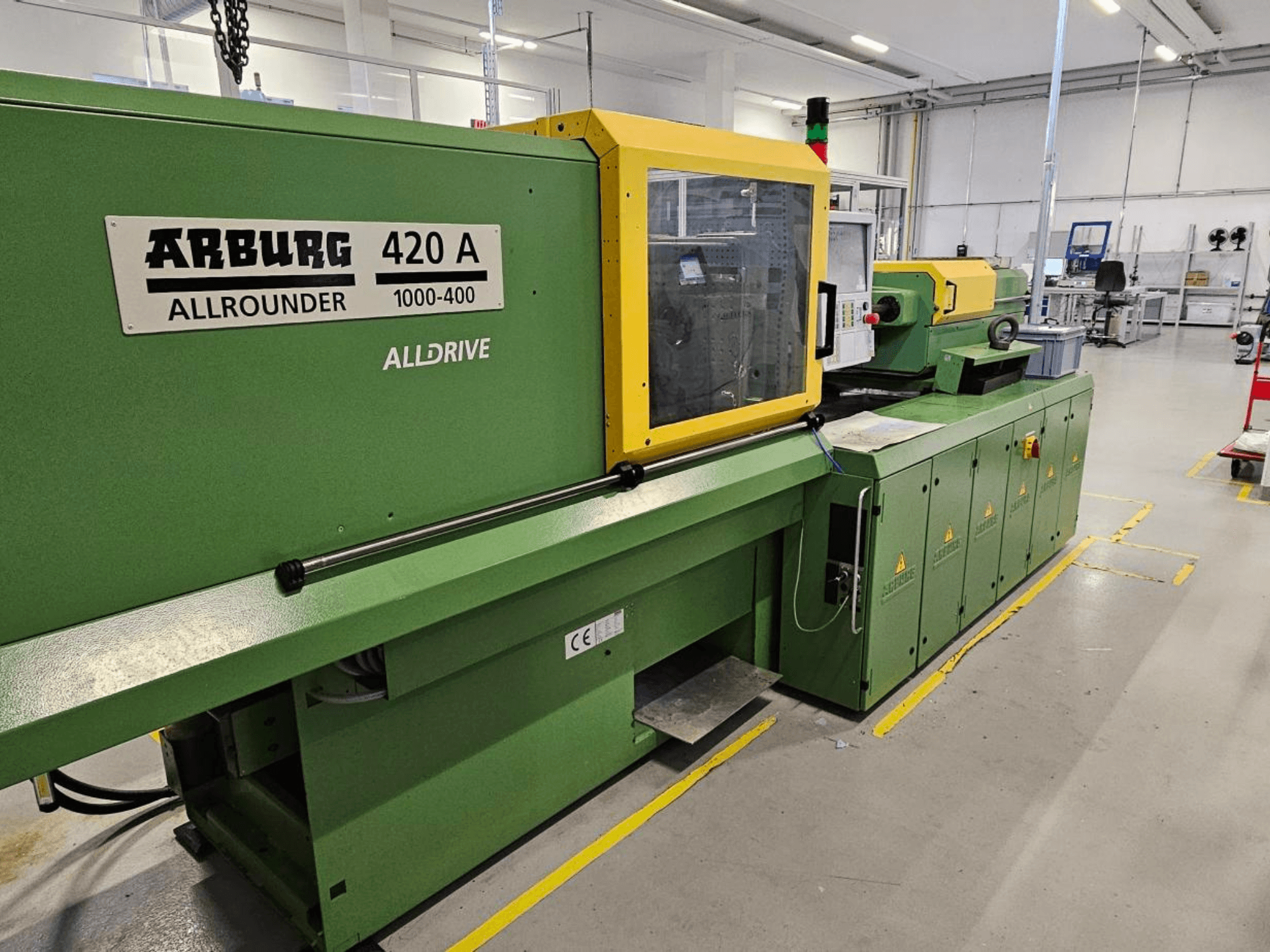ARBURG 420 A Allrounder 1000-400, vaizdas iš priekio; žalia mašina su geltonu skydeliu, jutikliniu ekranu ir saugos funkcijomis.