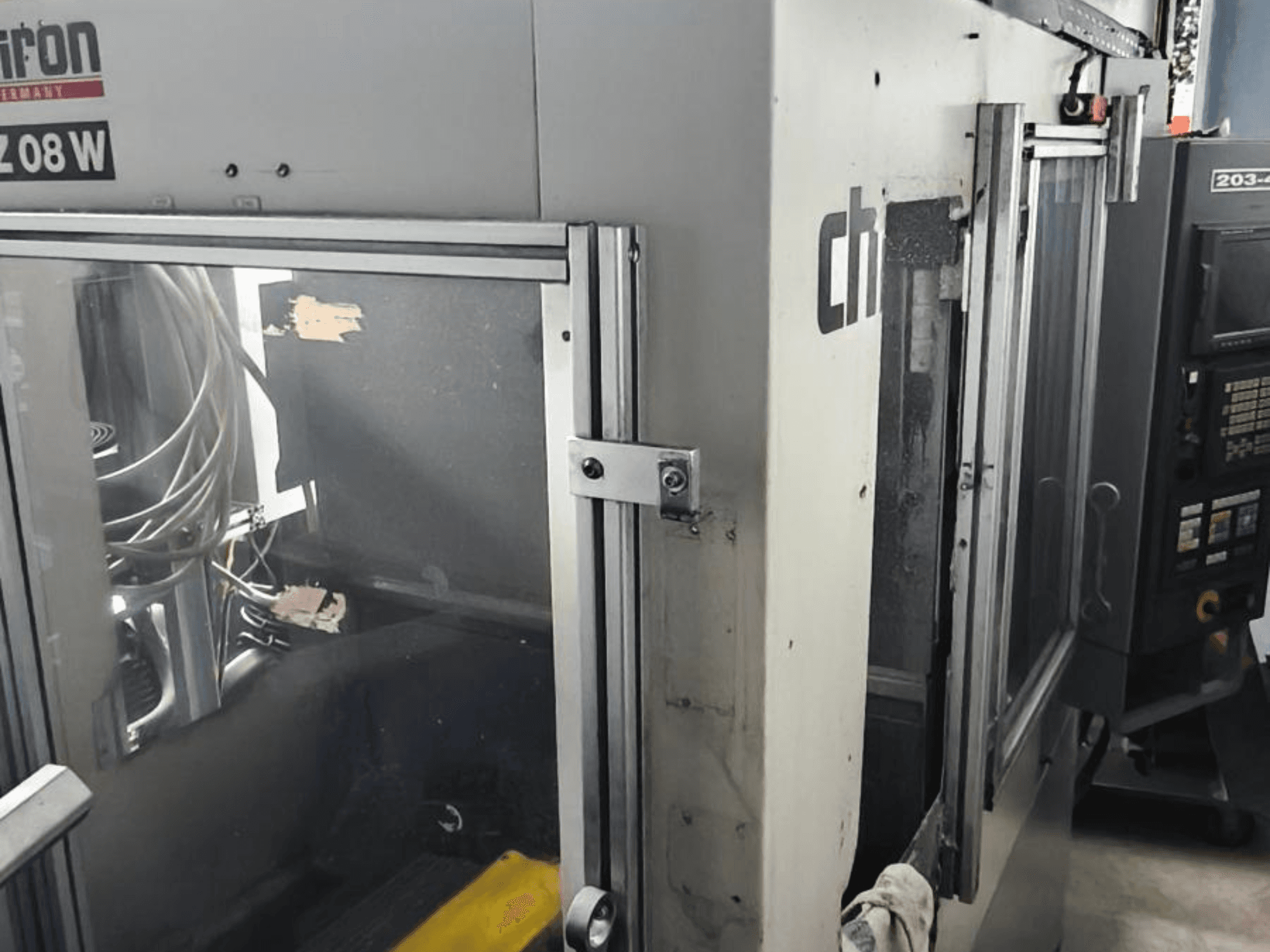 Vertikalaus apdirbimo centras CHIRON FZ 08 W, priekinis vaizdas, kuriame matyti valdymo skydelis ir iš dalies atidarytos durelės, su matomais vidiniais komponentais.