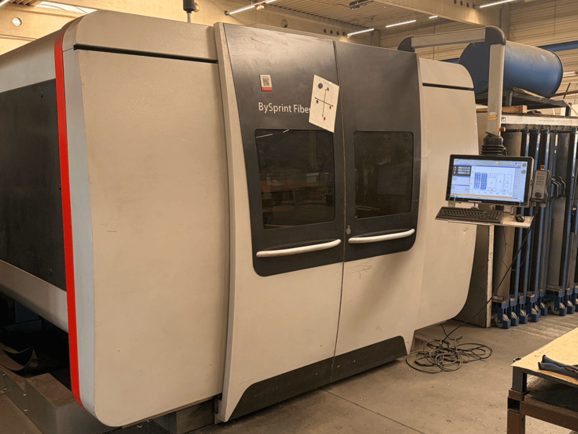 „Bystronic BySprint Fiber 3015“ – pluošto lazerio pjovimo staklių vaizdas iš priekio su jutikliniu valdymo skydeliu ir pramonine aplinka.