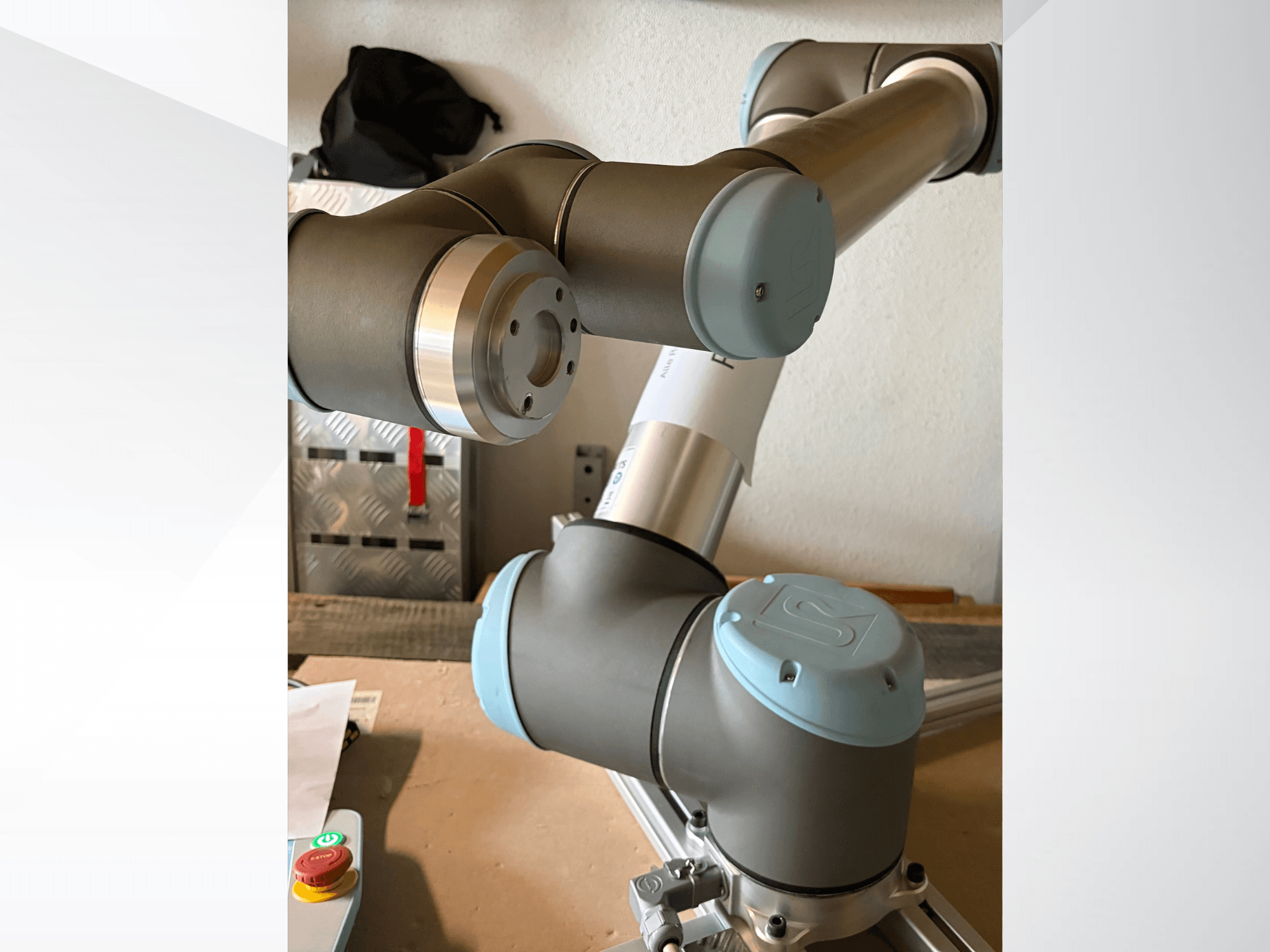 Roboto rankos "Universal Robots UR10" šoninis vaizdas iš arti, išryškinant sąnarius ir pilkai mėlynos spalvos konstrukcijos elementus.