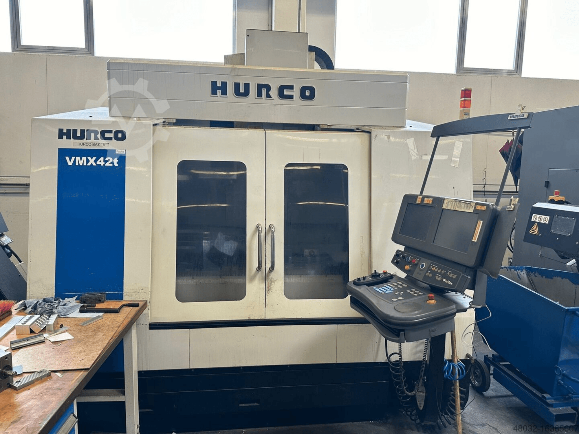 „Hurco VMX42t“ vertikalusis apdirbimo centras, vaizdas iš priekio, kuriame matomas valdymo pultas ir vidus su įrankiais bei apdirbamais ruošiniais.