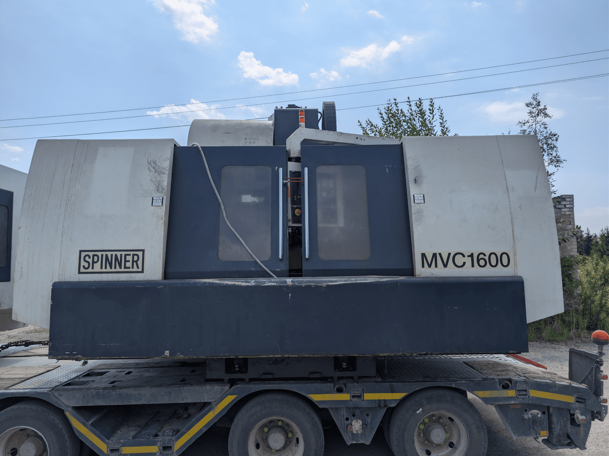 Vertikalus apdirbimo centras „SPINNER MVC 1600“, vaizdas iš priekio ant sunkvežimio, kuriame matyti prekės ženklas ir didelė apdirbimo zona.