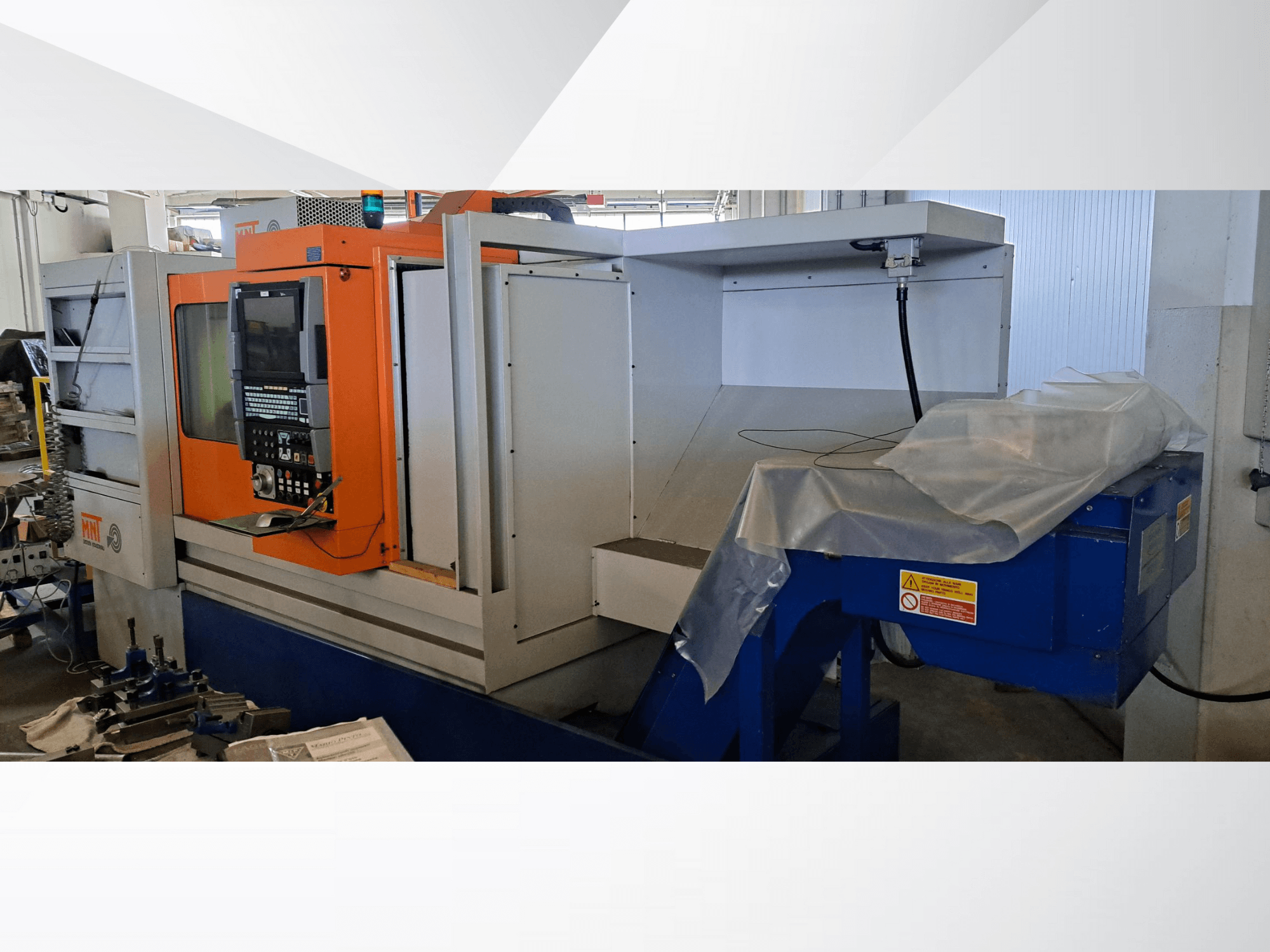 MNT CNC staklės, vaizdas iš priekio, oranžinis valdymo skydelis, didelis apdirbimo plotas ir mėlynas drožlių šalinimo įrenginys.