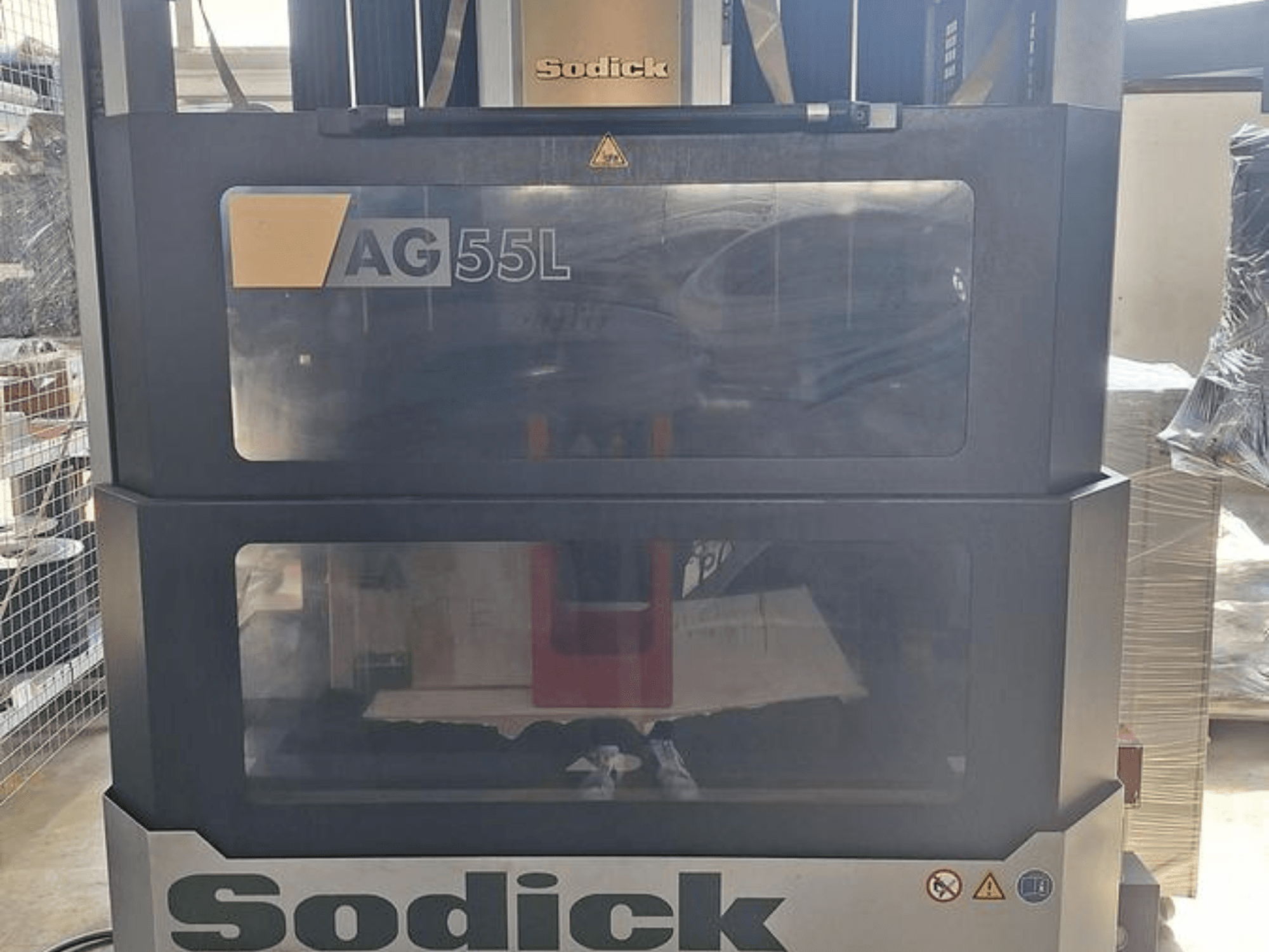 Sodick AG 55L štampavimo EDM staklės, vaizdas iš priekio, kai valdymo elementai matomi per permatomas plokštes ir matoma viduje esanti darbo vieta.