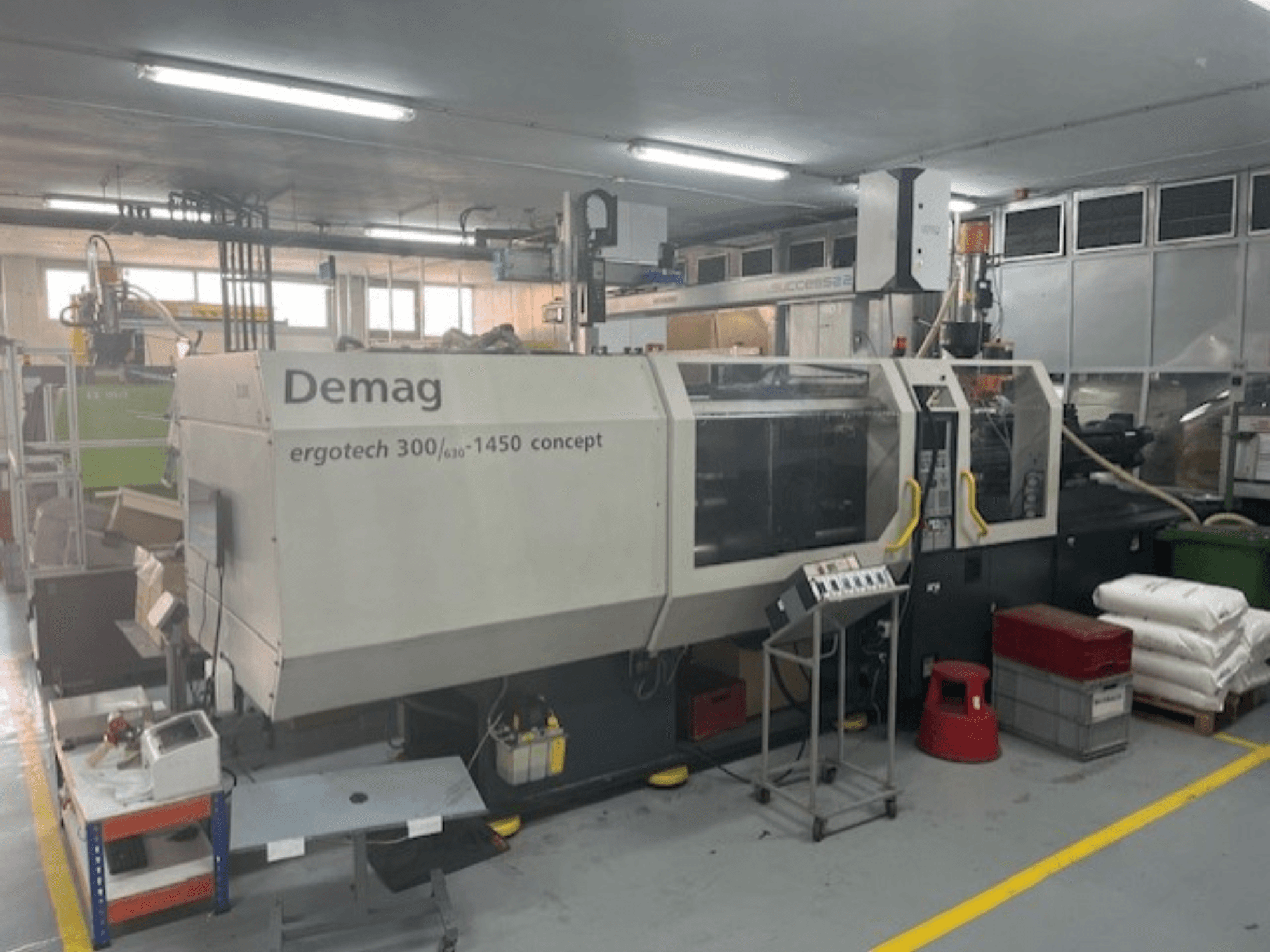 "Demag ERGOTECH CONCEPT 3000-1450" hidraulinė liejimo mašina, vaizdas iš priekio, su valdymo įtaisais ir šalia esančiomis medžiagomis.