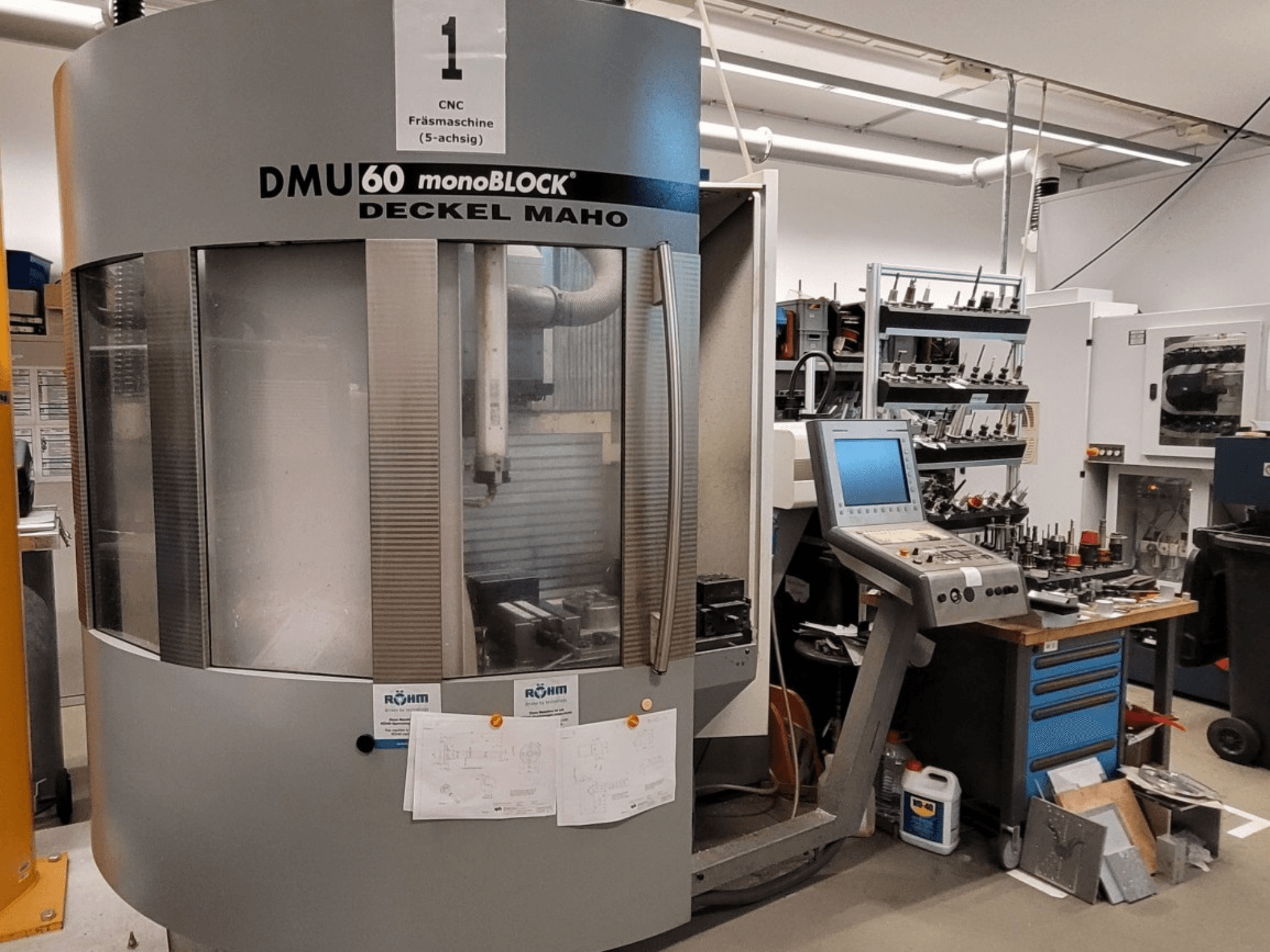 CNC frezavimo staklės DECKEL MAHO DMU 60 monoBLOCK iš priekio, matomas valdymo skydelis ir įrankių saugykla šalia jo.