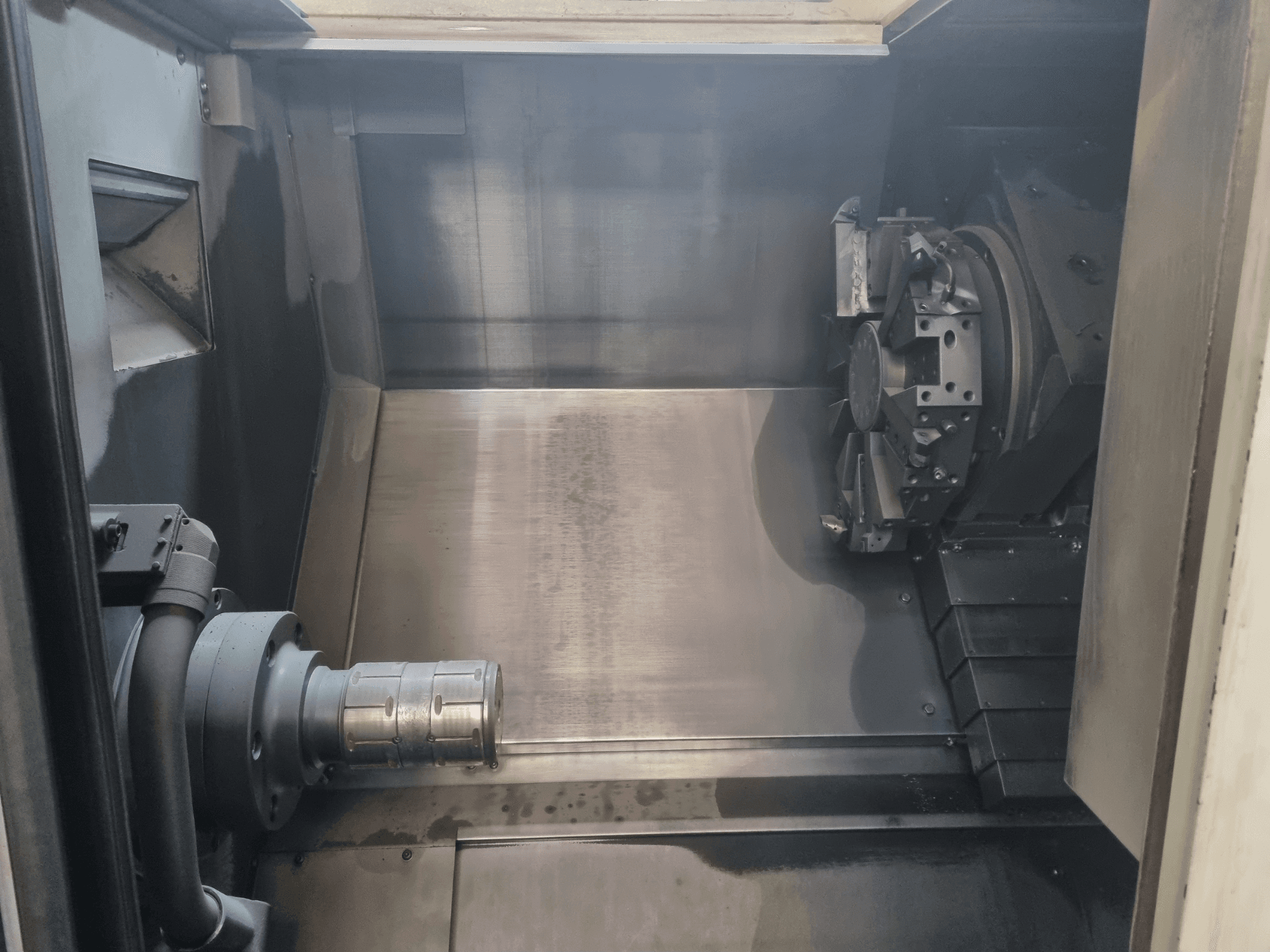 CNC staklių interjero vaizdas, kuriame matyti metalinė darbo zona, įrankių laikiklis ir griebtuvas; pabrėžiamas inžinerinis tikslumas.