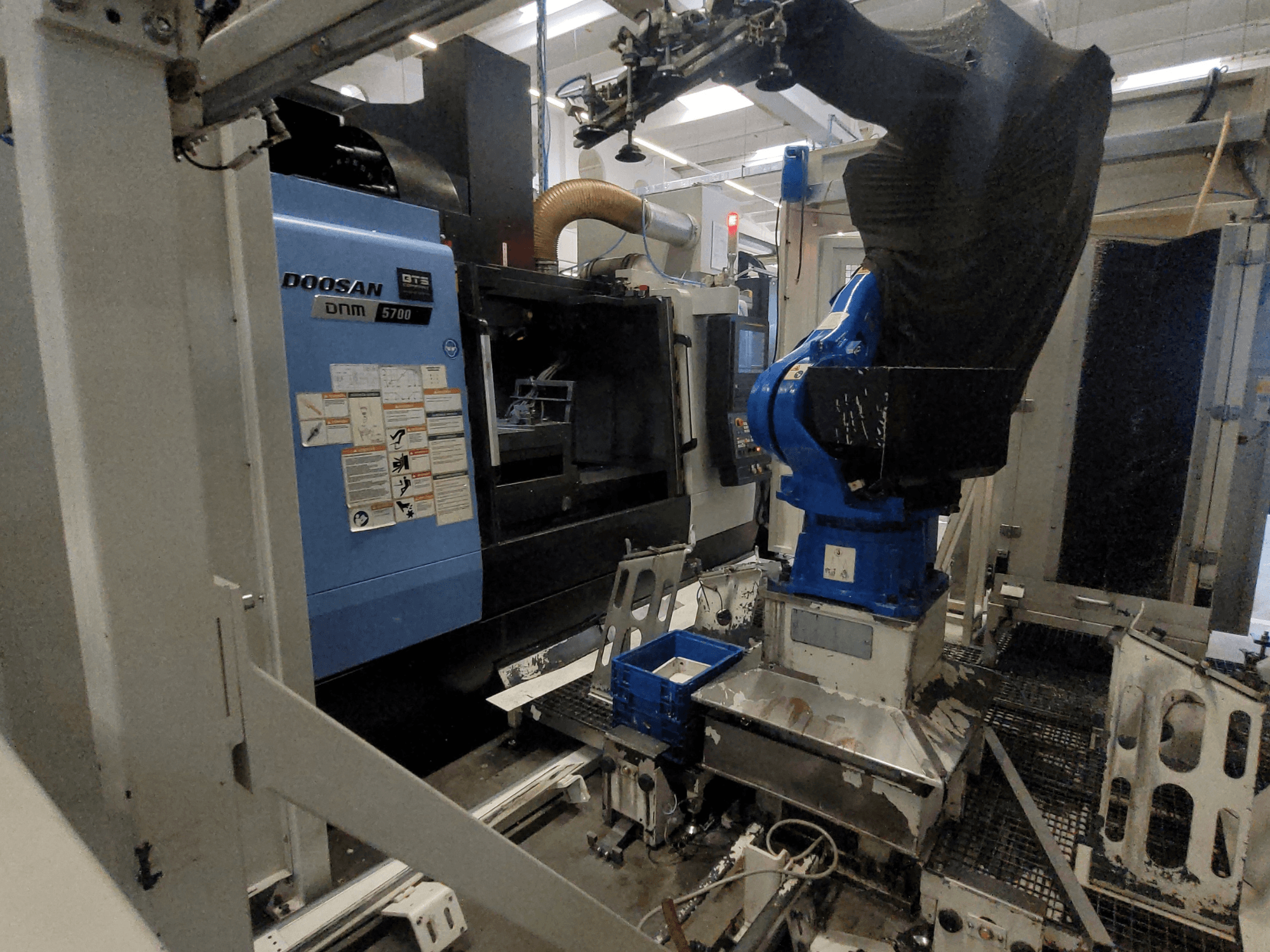 „DOOSAN DNM 5700“ vertikalusis apdirbimo centras gamykloje: matomas jo vaizdas iš priekio ir integruota robotinė ranka.
