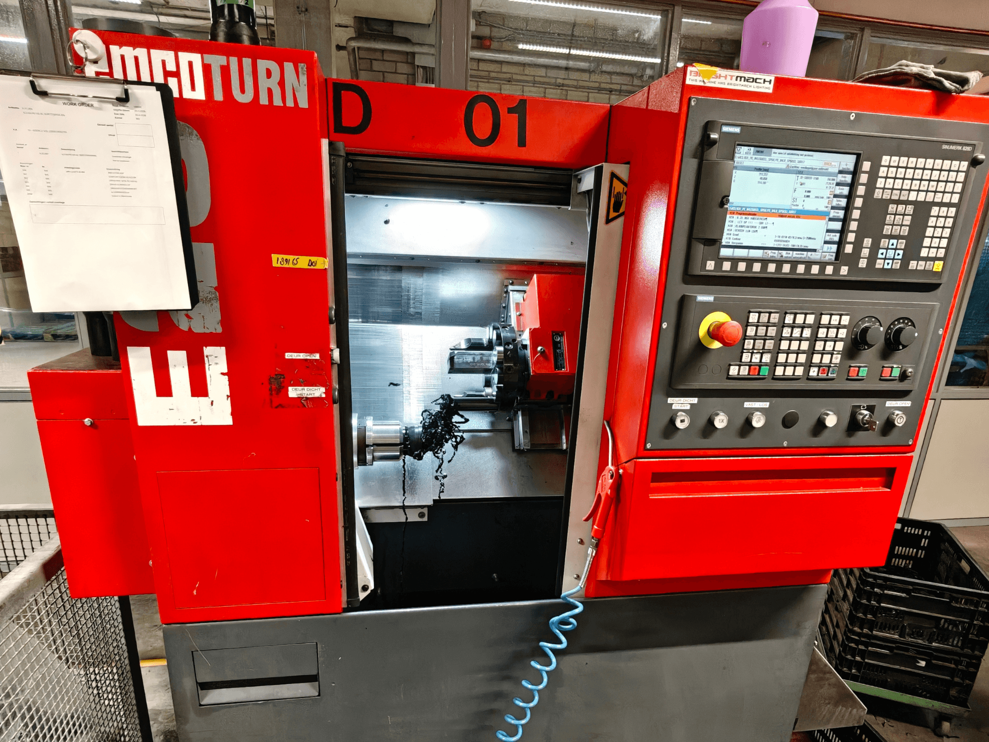 Horizontaliųjų tekinimo staklių EMCO TURN E25 vaizdas iš priekio, kuriame matomi valdymo įtaisai, įrankių laikiklis ir darbo zona su drožlėmis.