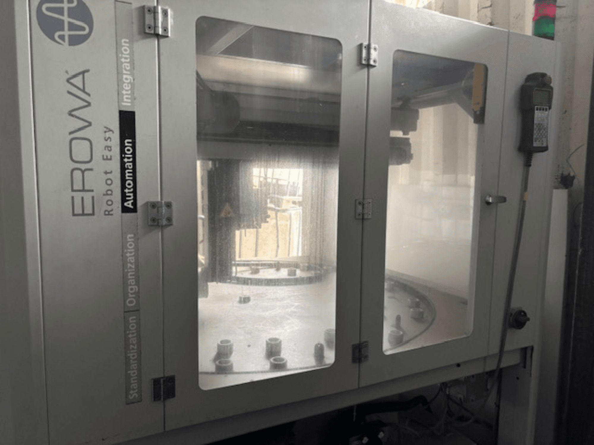 "EROWA Robot Easy Automation" vaizdas iš priekio; skaidrios durys, matomi automatikos komponentai ir valdymo skydelis.