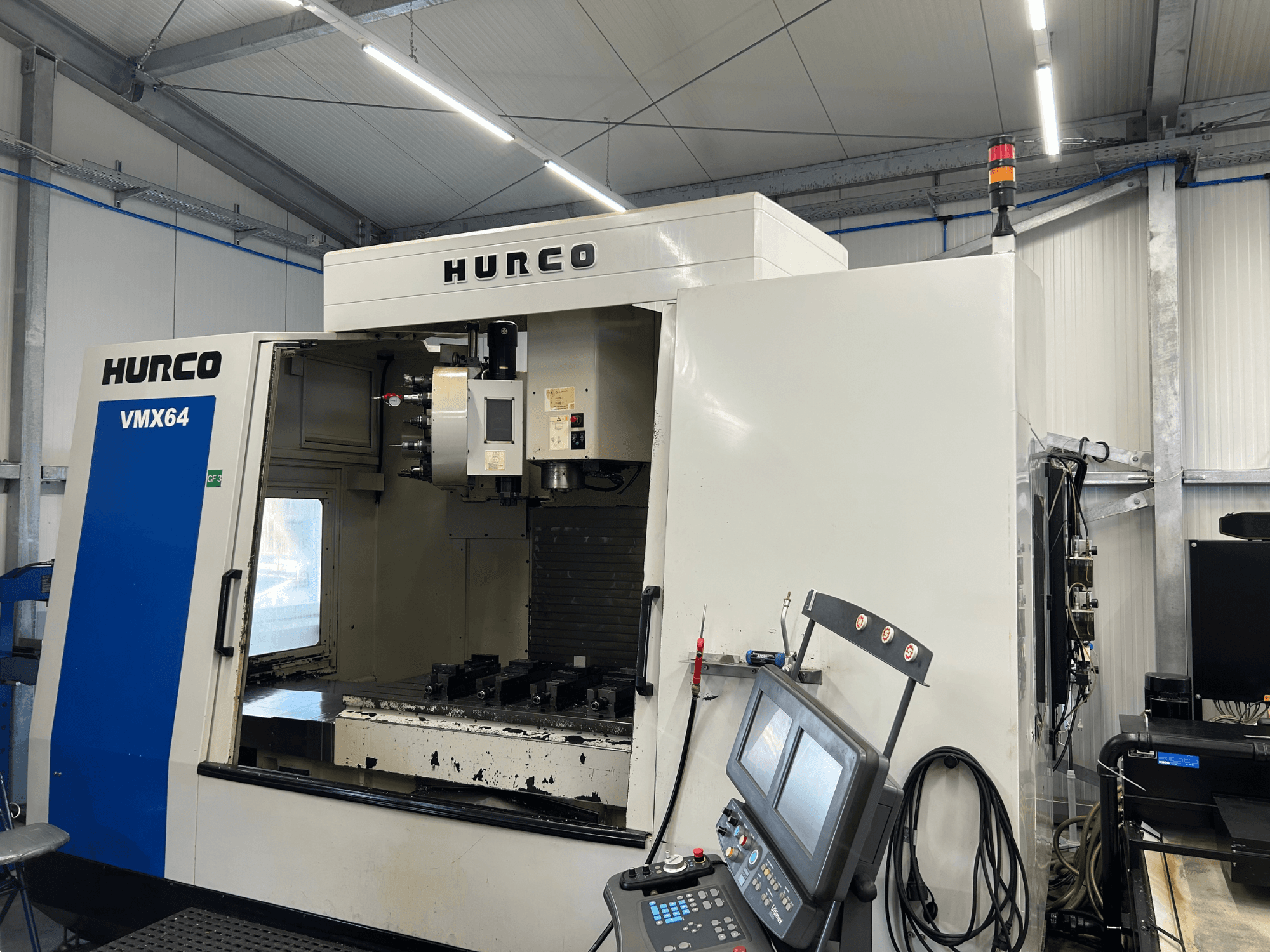 Vertikalusis apdirbimo centras „Hurco VMX 64“, vaizdas iš priekio, kuriame matomas valdymo pultas ir atvira darbo erdvė su įrankiais.