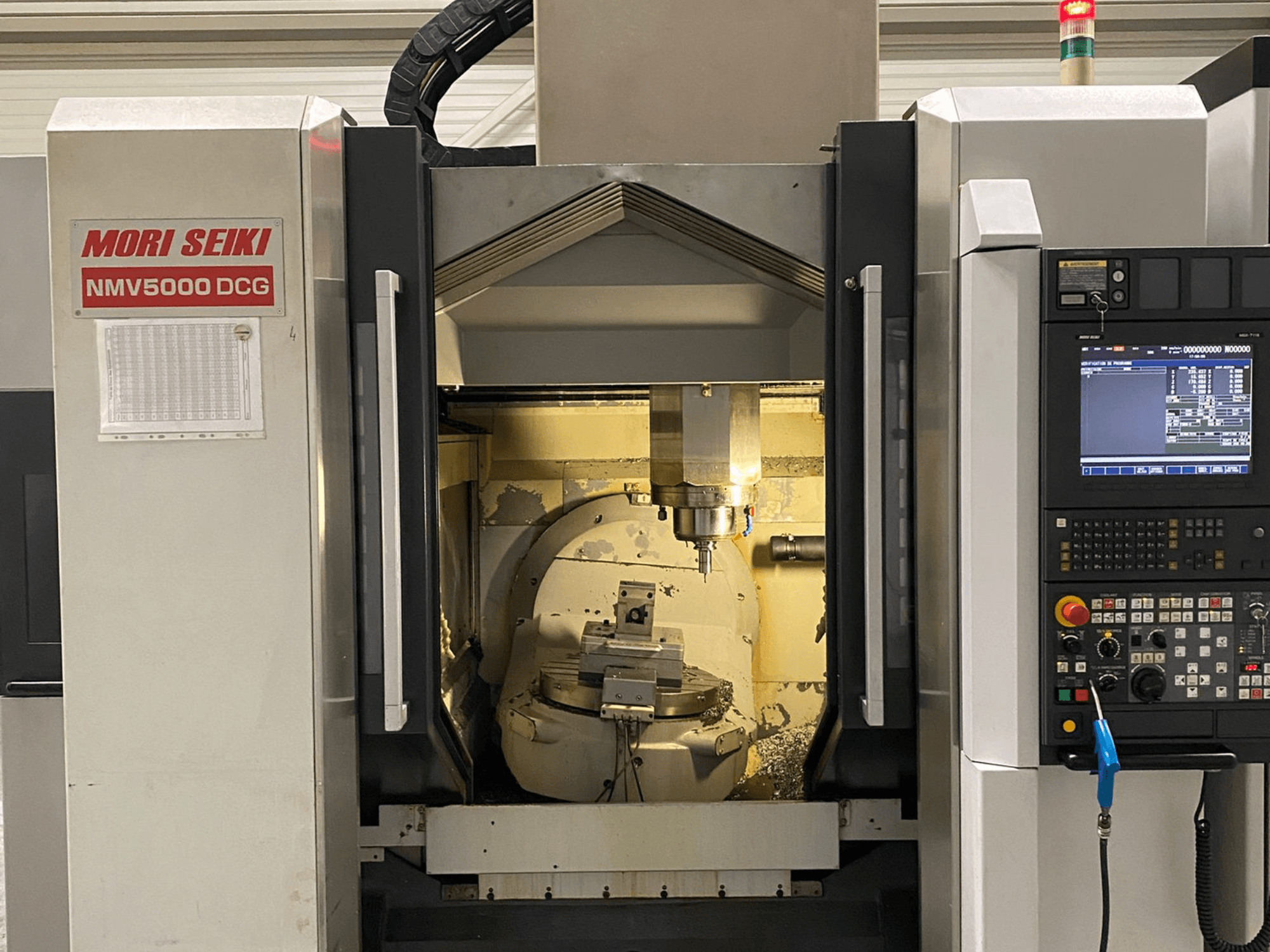 MORI SEIKI NMV 5000DCG universalus apdirbimo centras, priekinis vaizdas, kuriame matomas valdymo skydelis ir vidinė apdirbimo zona.