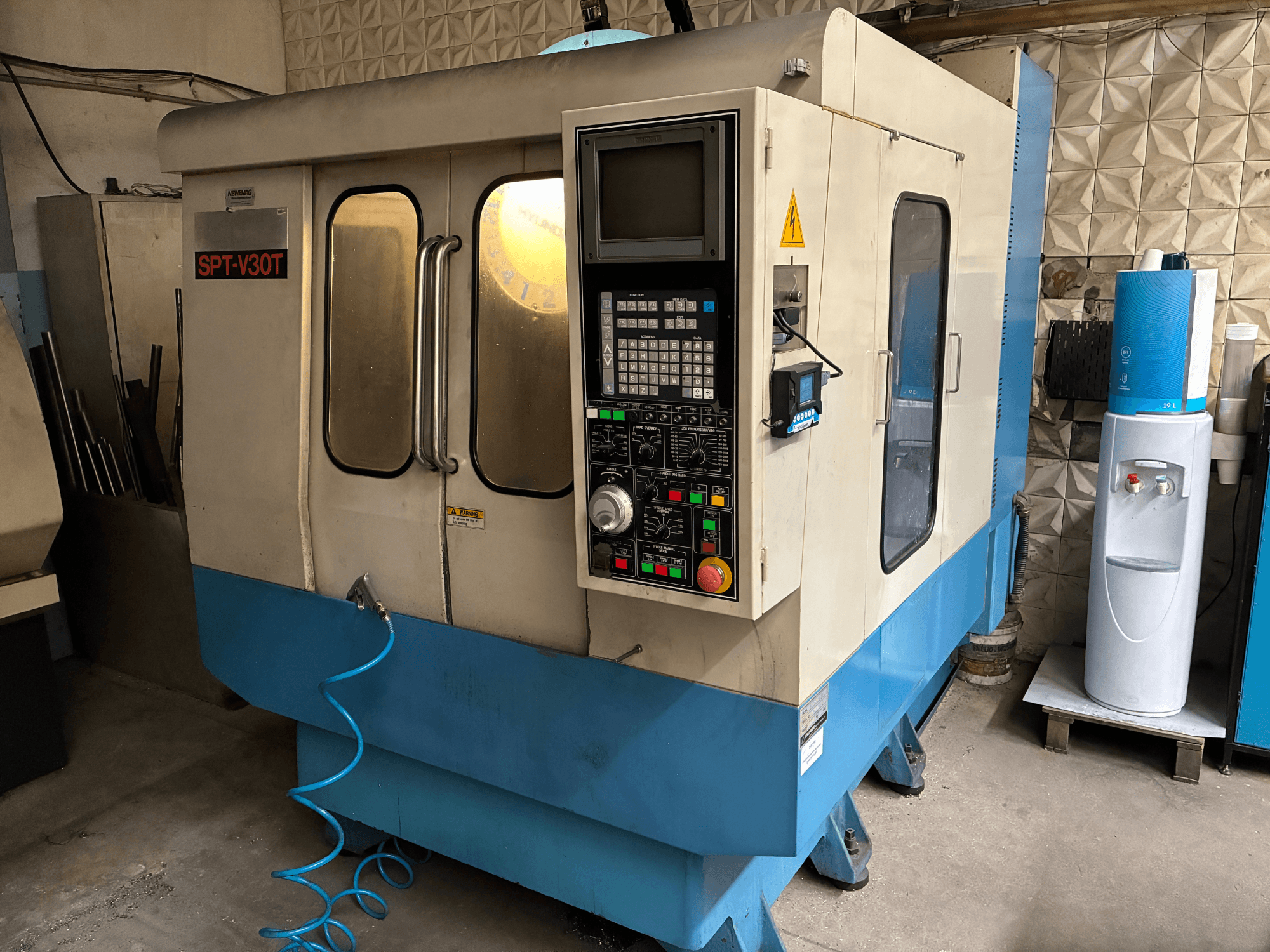 SPT-V30T CNC staklės mėlyna ir balta spalvomis, priekinis vaizdas, kuriame matyti valdymo skydelis, durelės ir oro tiekimo žarna. Puikiai tinka tiksliam apdirbimui.