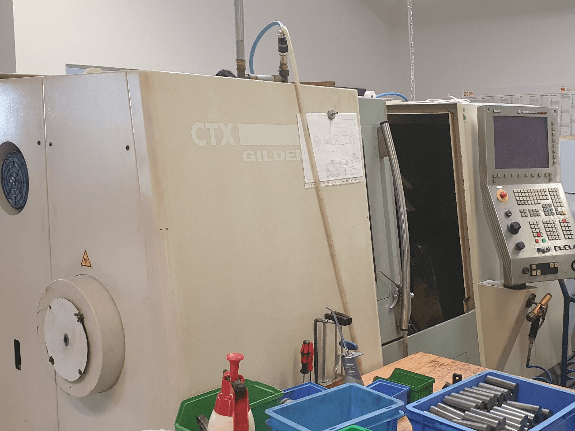 DMG GILDEMEISTER CTX 310 horizontalaus tekinimo staklių vaizdas iš priekio, matomas valdymo pultas, pirmoje plane – įrankiai ir talpyklos.
