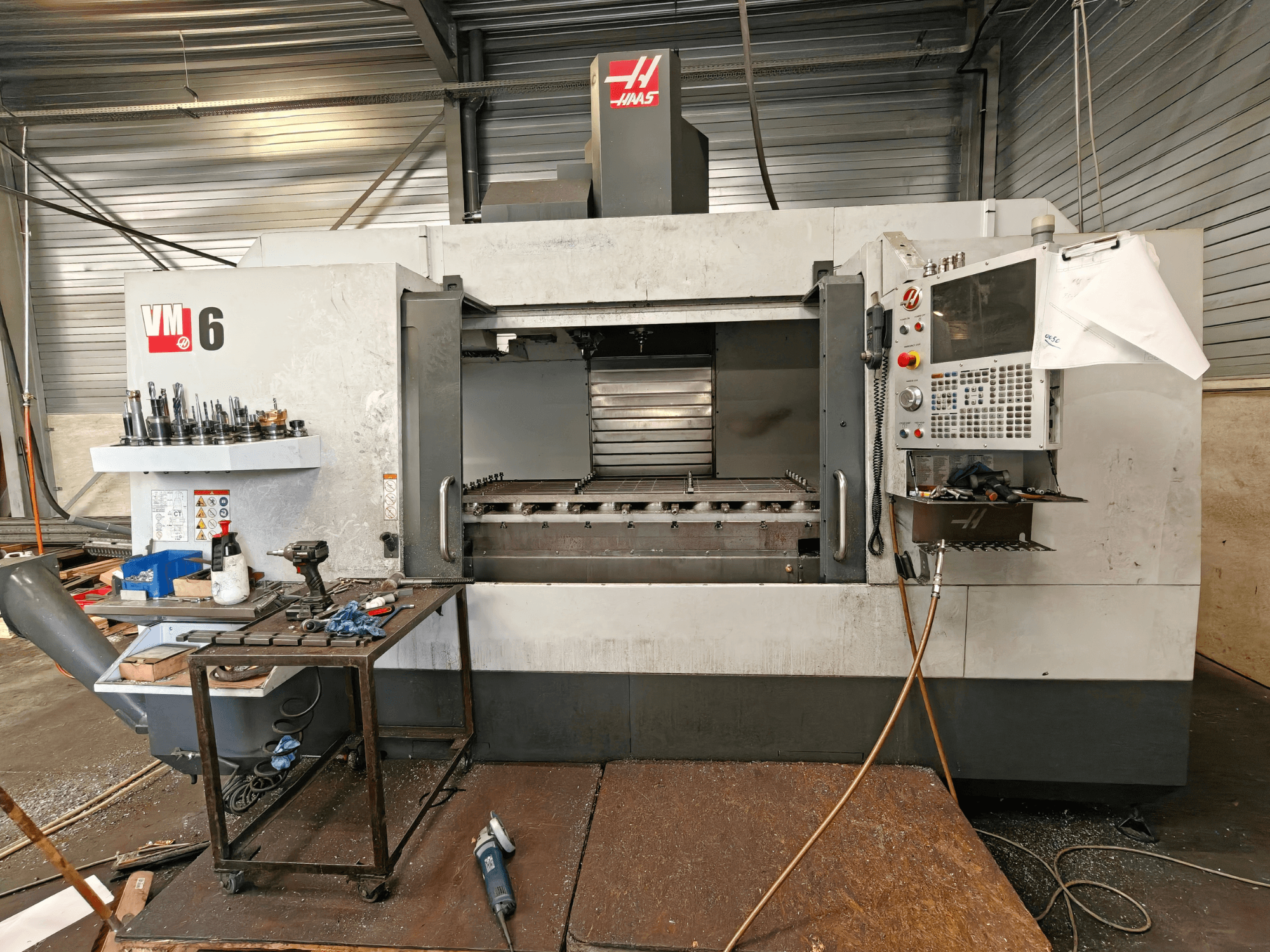 Vertikalusis apdirbimo centras „Haas VM-6“, vaizdas iš priekio, matyti įrankių saugykla, valdymo pultas ir darbo zonoje esantys nuolaužos.