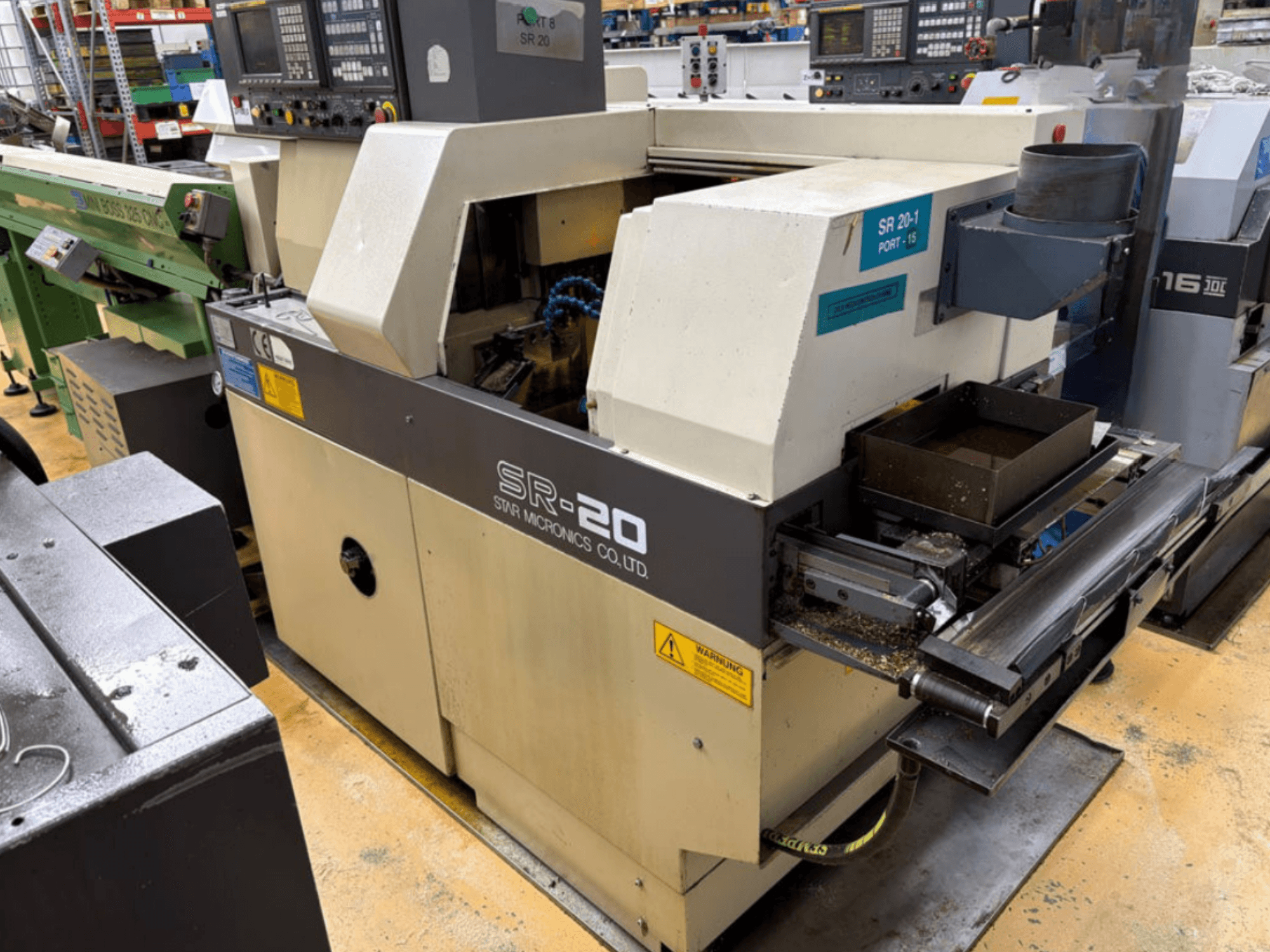 „STAR MICRONICS SR20“ šveicariško tipo tekinimo staklių šoninis vaizdas, kuriame matomas valdymo pultas ir įrankių zona su drožlėmis.