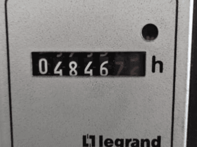 "Legrand" valandų skaitiklis, rodantis 048467.6, vaizdas iš priekio, raudona kontrolinė lemputė ir juodi skaitmenys šviesiame tekstūriniame fone.
