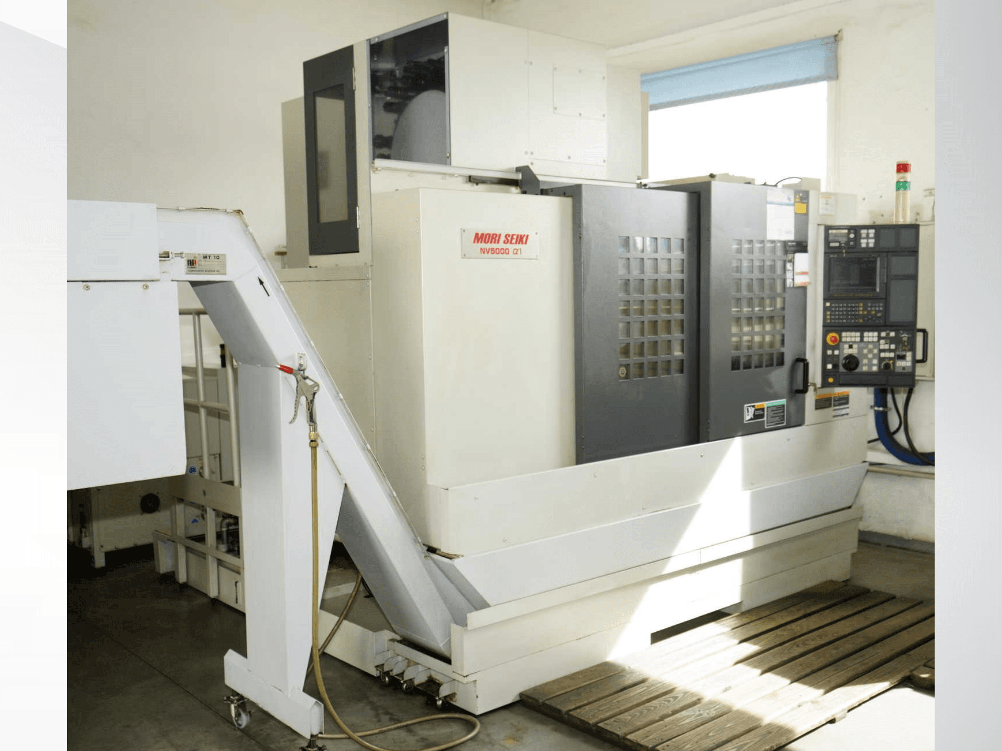 MORI SEIKI NV 5000 alpha1 vertikaliojo apdirbimo centras, vaizdas iš priekio, kuriame matomas valdymo pultas, saugos įranga ir krovimo zona.
