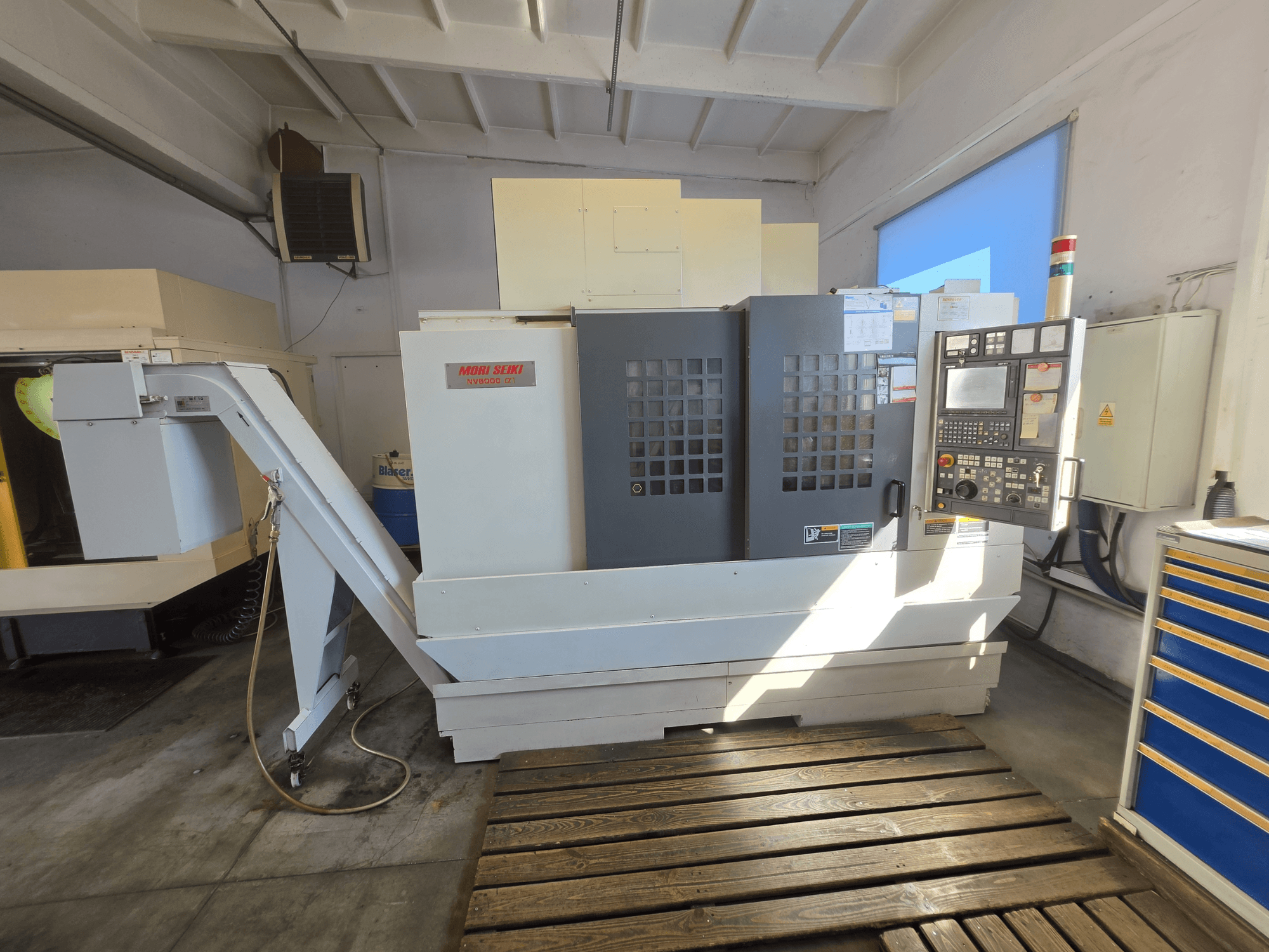 Vertikalusis apdirbimo centras „MORI SEIKI NV 5000 alpha1“, vaizdas iš priekio, kuriame matomas valdymo skydas ir staklių funkcijos dirbtuvės aplinkoje.