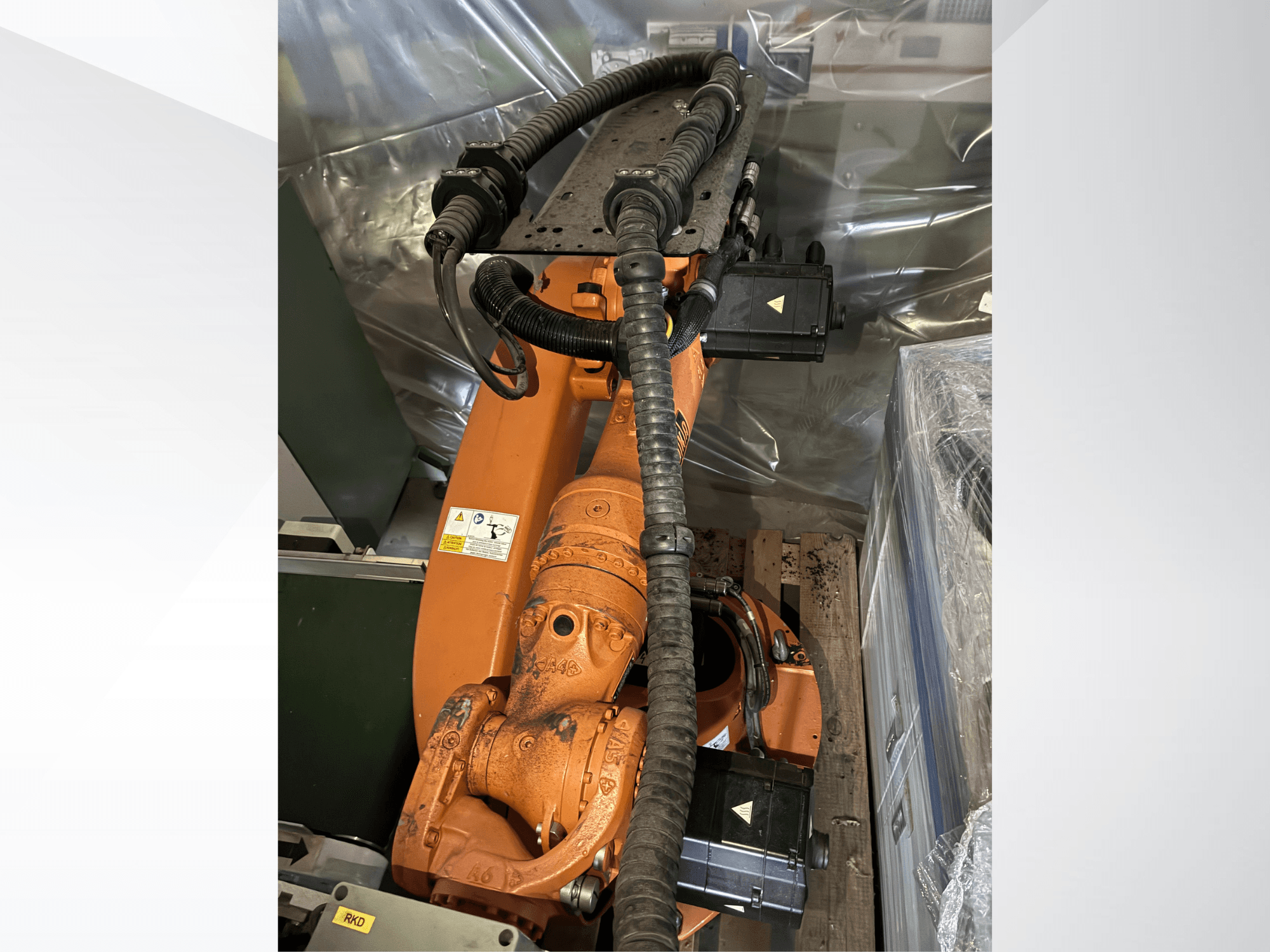 Oranžinės spalvos „KUKA KR16-2“ roboto ranka, vaizdas iš viršaus, kuriame matomi jungtys ir apsauginiai vamzdeliai.