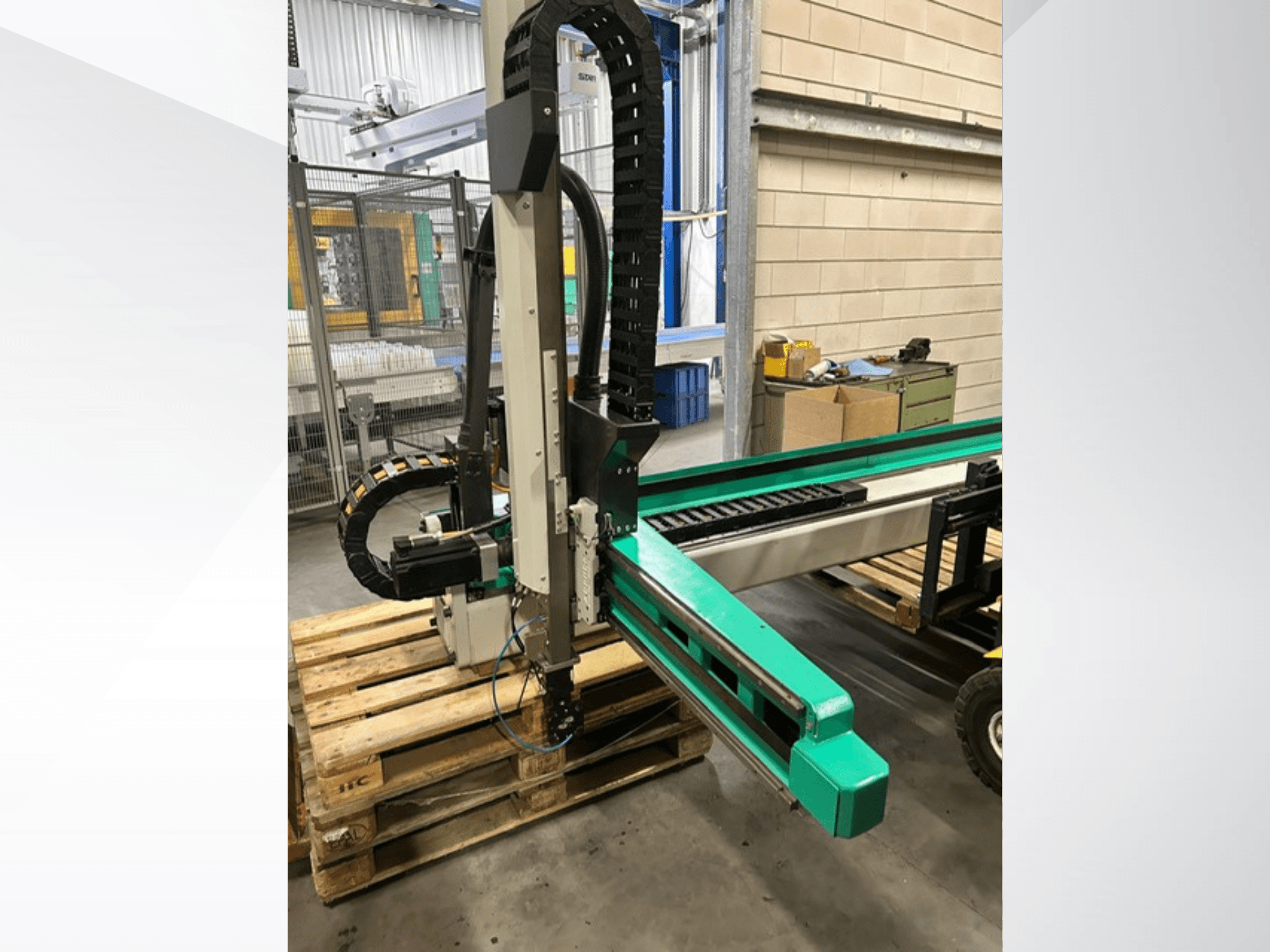 "Arburg Multilift Select 15 kg quer", šoninis vaizdas, kuriame matoma ant medinių padėklų sukrautų ruošinių tvarkymo sistema, rodomos roboto rankos ir valdymo komponentai.