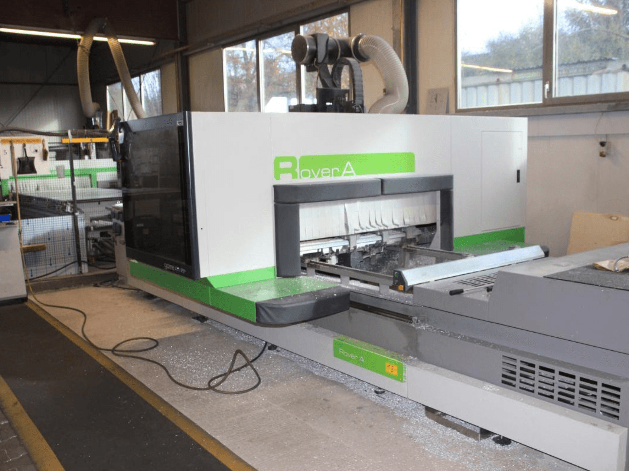 BIESSE Rover A 1232 CNC maršrutizatorius, šoninis vaizdas, rodantis pjovimo zoną ir valdymo skydelį pramoninėje aplinkoje.