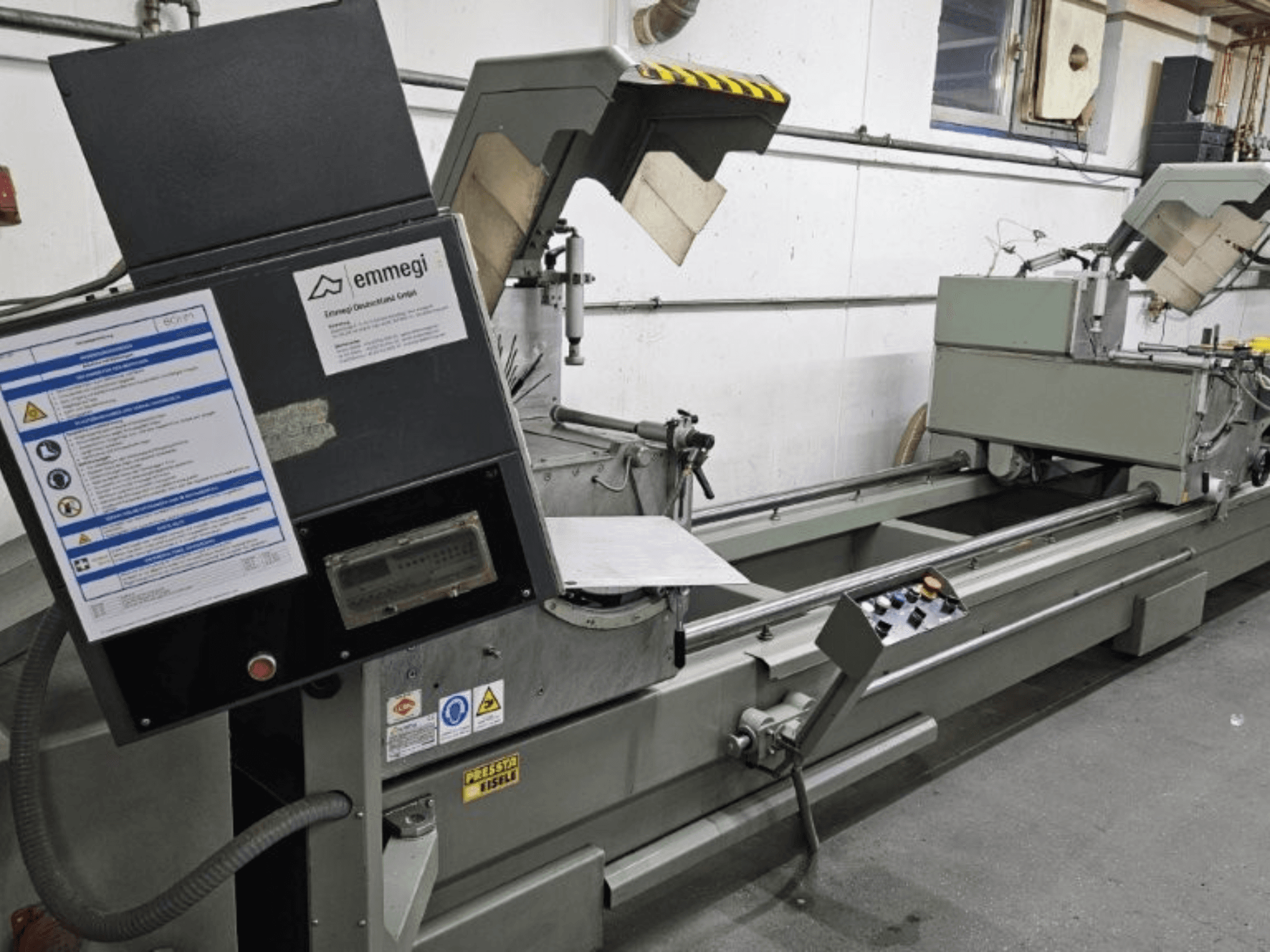 "Emmegi" pramoninės pjaustymo staklės, vaizdas iš priekio, valdymo skydelis, saugos etiketės ir darbiniai komponentai.