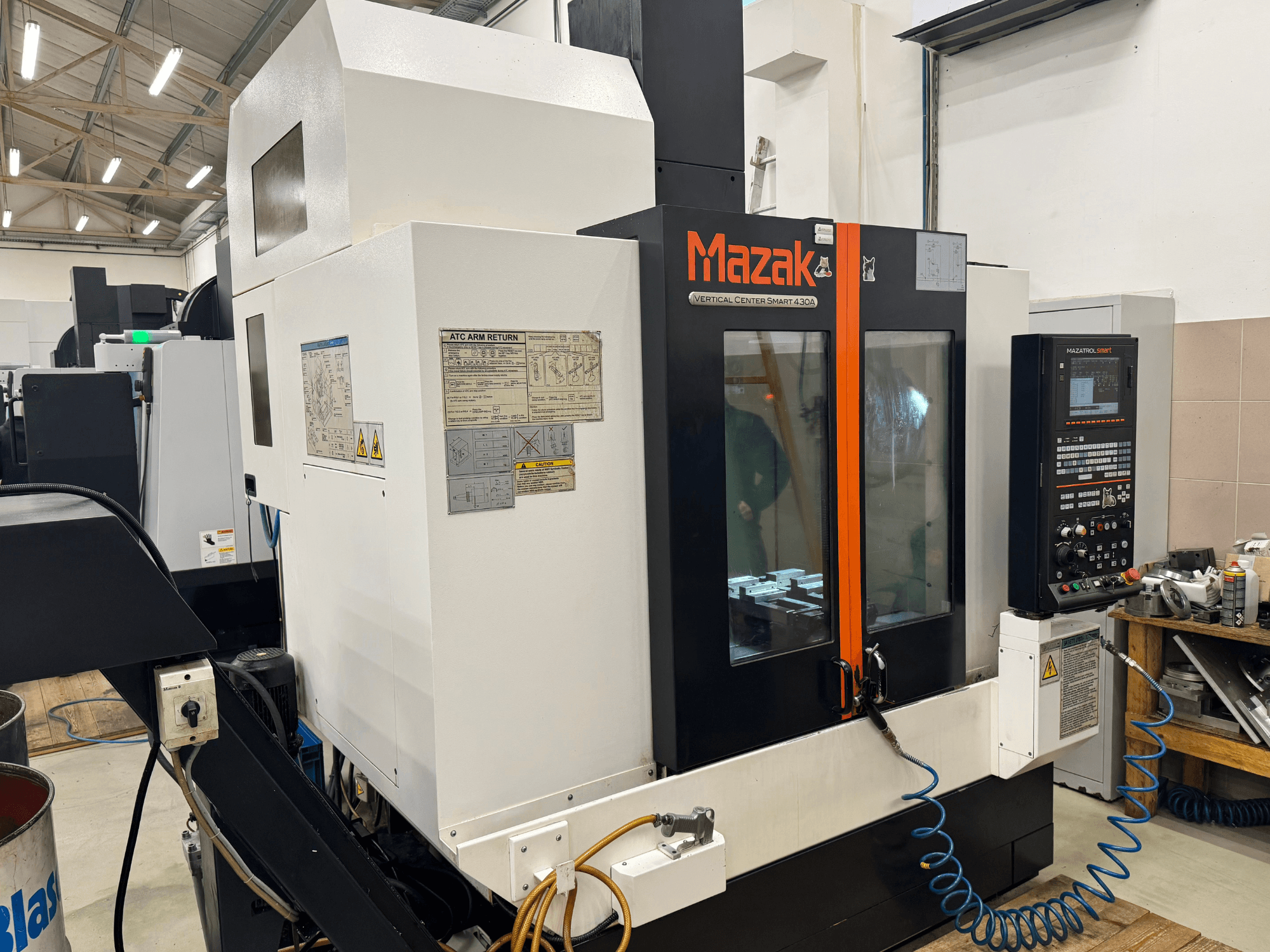 "Mazak Vertical Center Smart 430A", vaizdas iš priekio; CNC frezavimo staklės su valdymo skydeliu, skaidriu korpusu ir matomu įrankių laikikliu.
