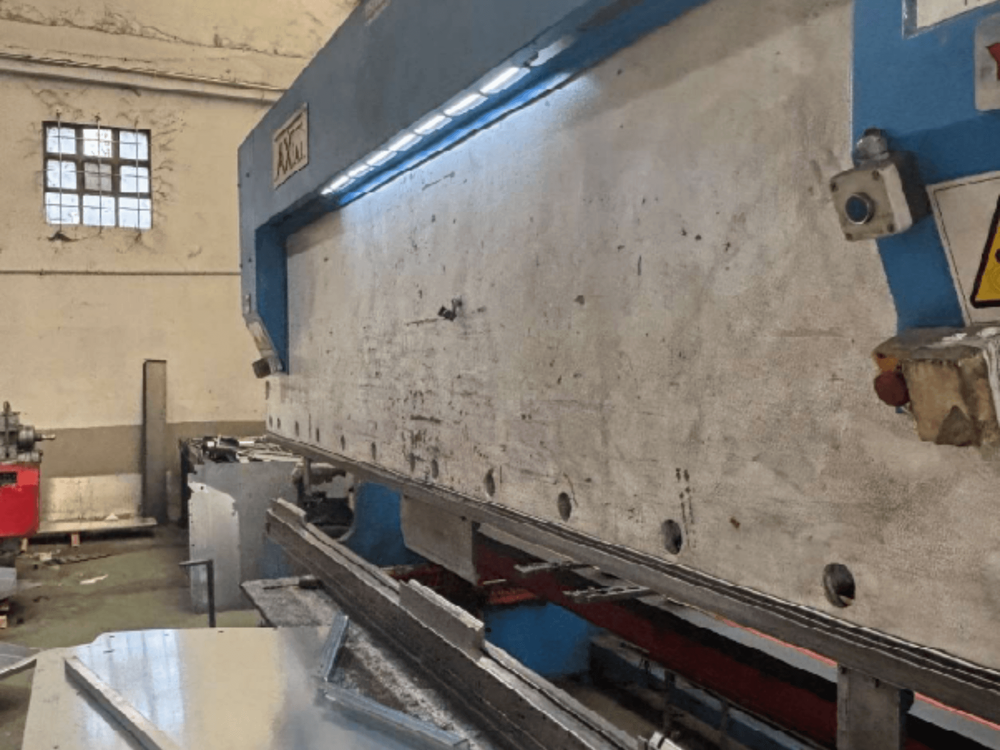 Axial PHS-W-124 padėklų tvarkymo sistema dirbtuvėse, šoninis vaizdas, kuriame matomas darbinis paviršius ir valdymo skydo detalės.