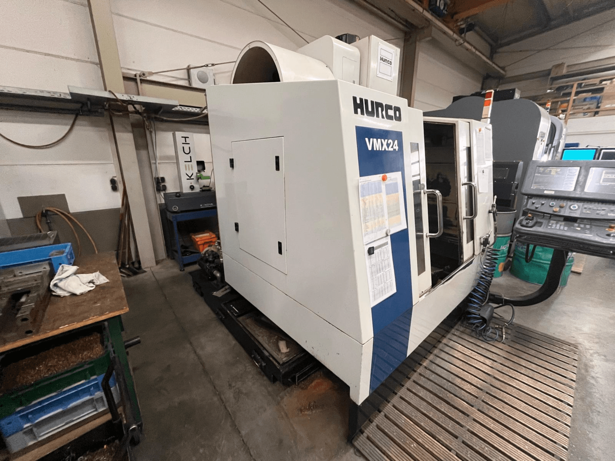 Hurco VMX24 CNC staklės dirbtuvėse, vaizdas iš priekio; yra valdymo skydelis ir atviros prieigos durys.
