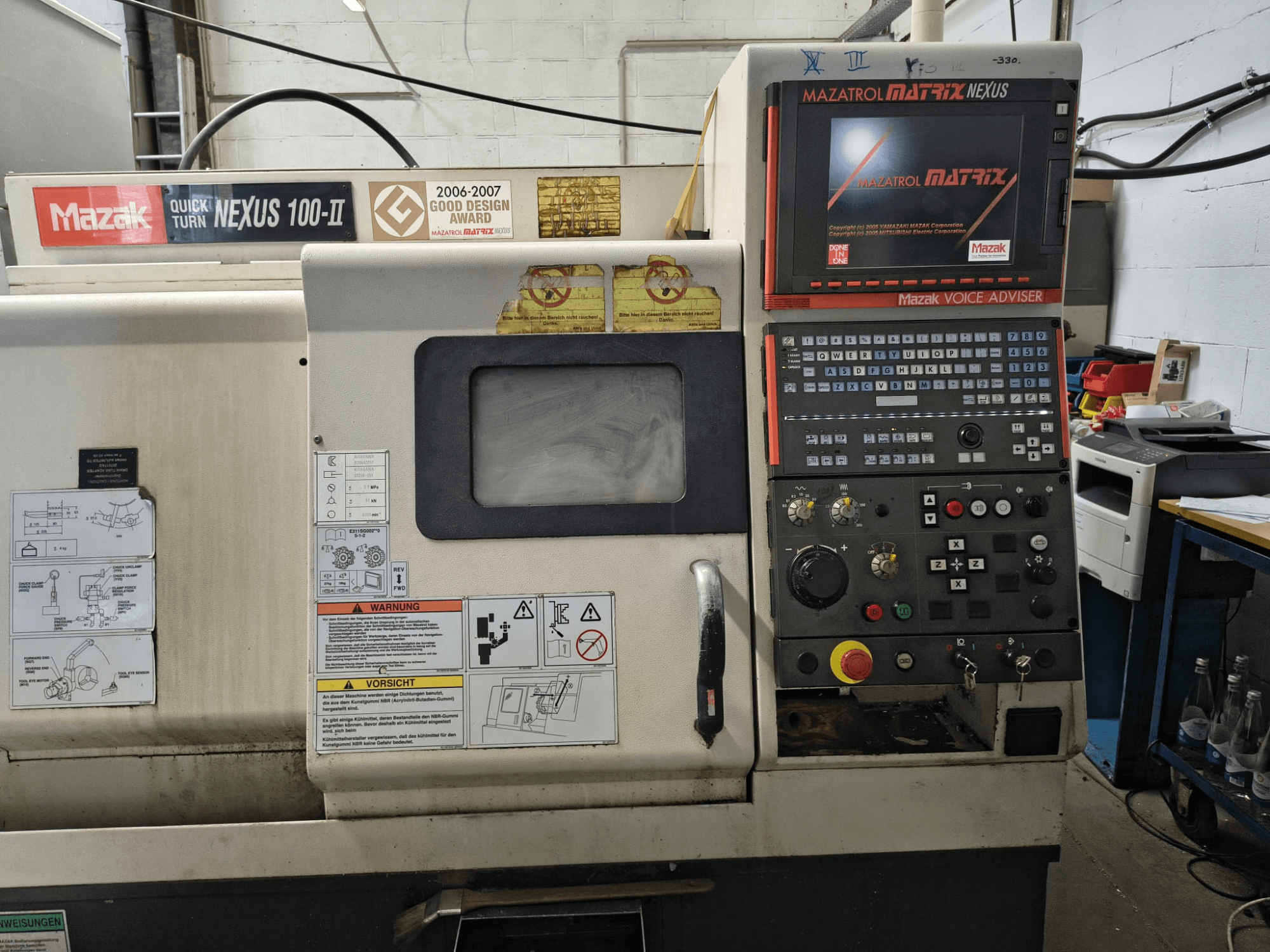 „Mazak Quick Turn Nexus 100-II“ horizontalaus tekinimo staklių vaizdas iš priekio, kuriame matomas valdymo pultas ir ekranas su techniniais duomenimis.