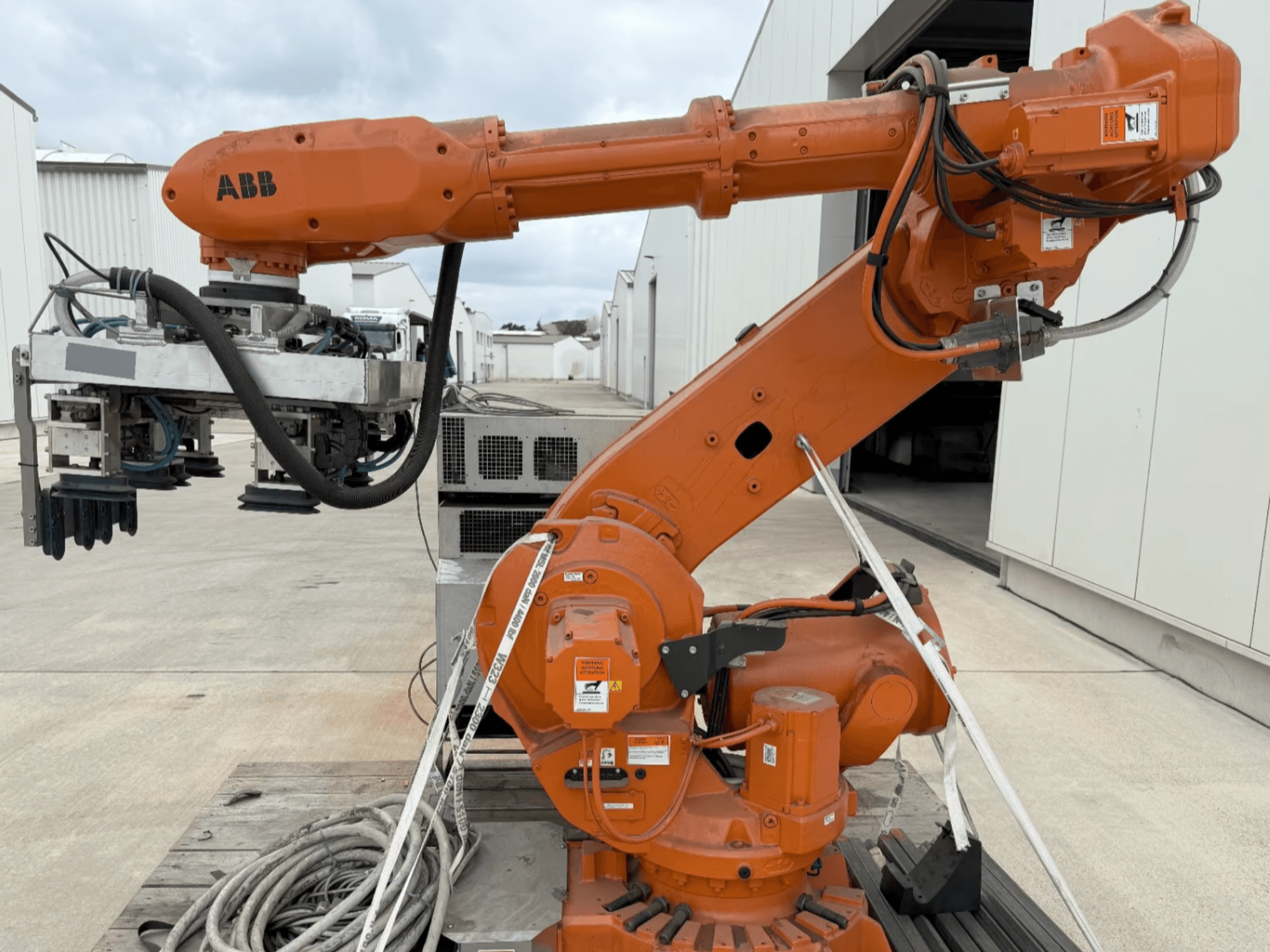 ABB RB 6600-130/3.2 roboto rankos šoninis vaizdas, kuriame matoma oranžinė roboto ranka su griebtuvo priedu ir matomais laidais.