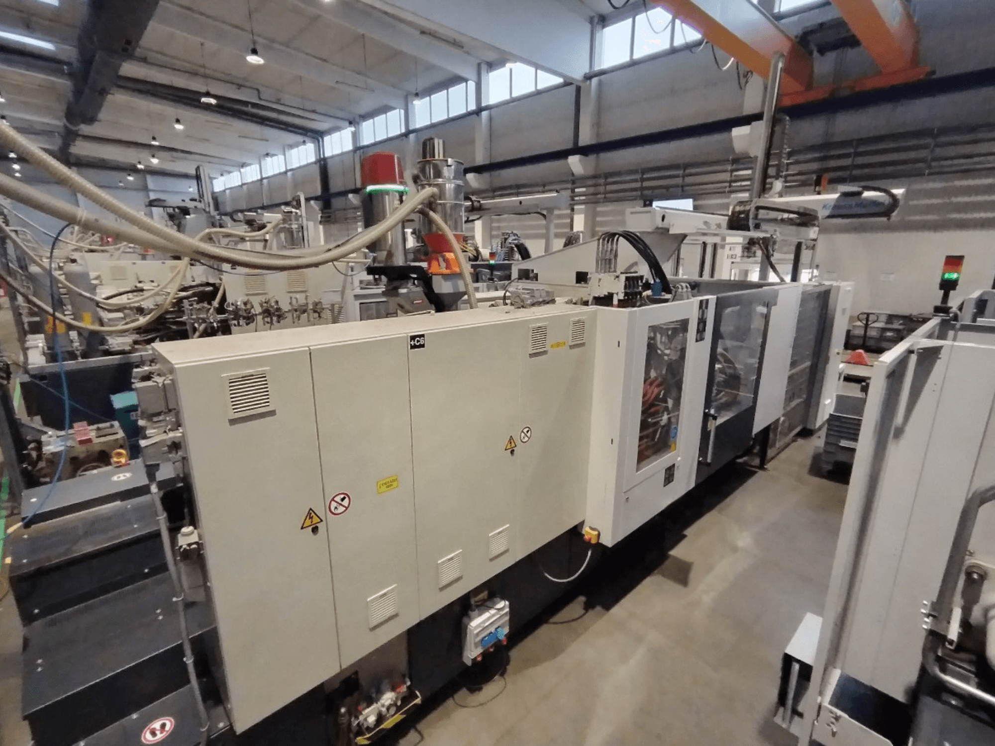 Pramoninė įpurškimo liejimo mašina, parodyta iš šono, su valdymo skydeliu ir saugos įspėjimais. Prekės ženklas: Nežinomas.