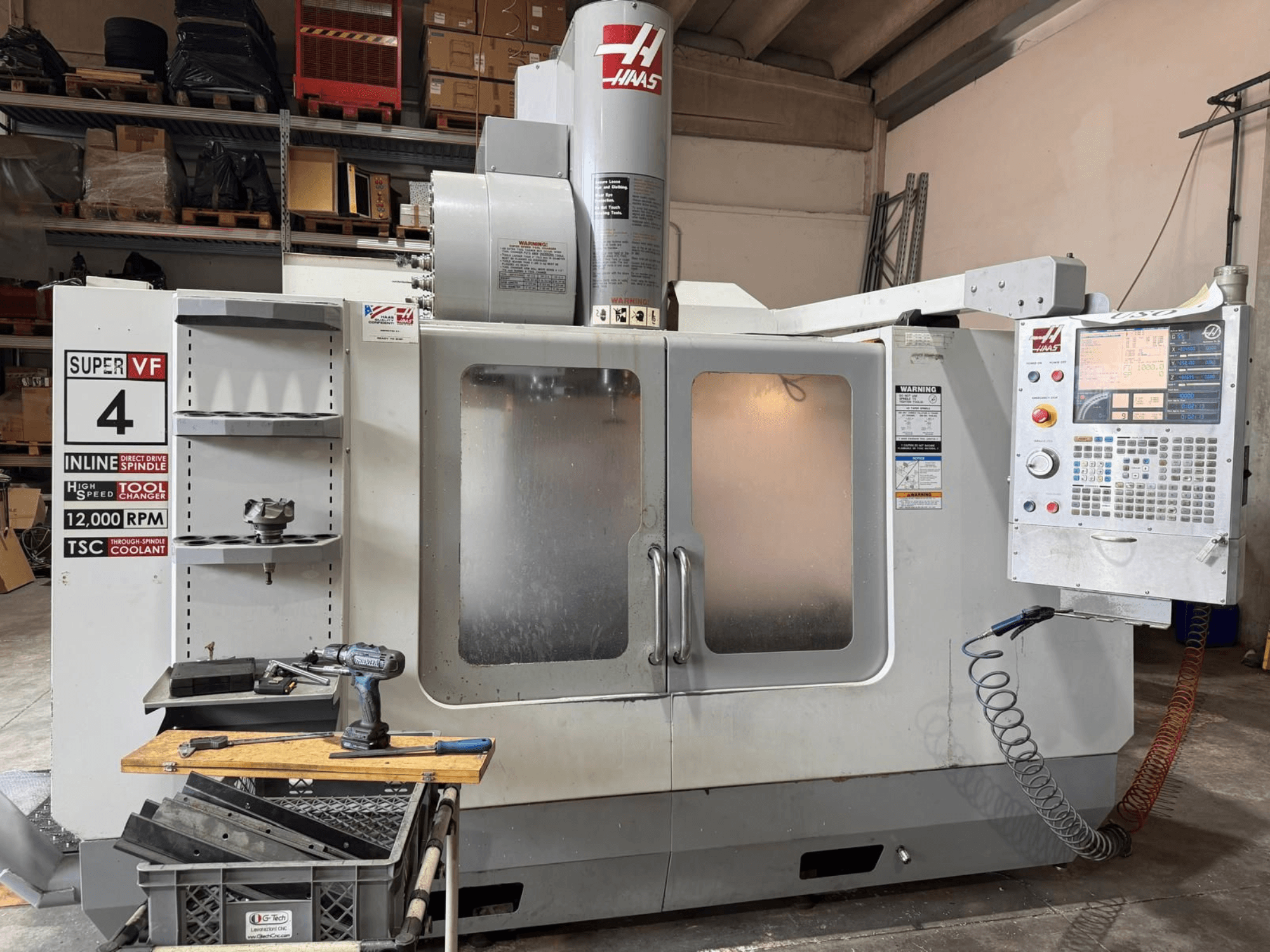 HAAS VF-4SSHE vertikaliojo apdirbimo centro vaizdas iš priekio su valdymo pultu, įrankių laikikliu ir 12 000 apsisukimų per minutę greičio suklio; greitaeigė, tiksli staklė.