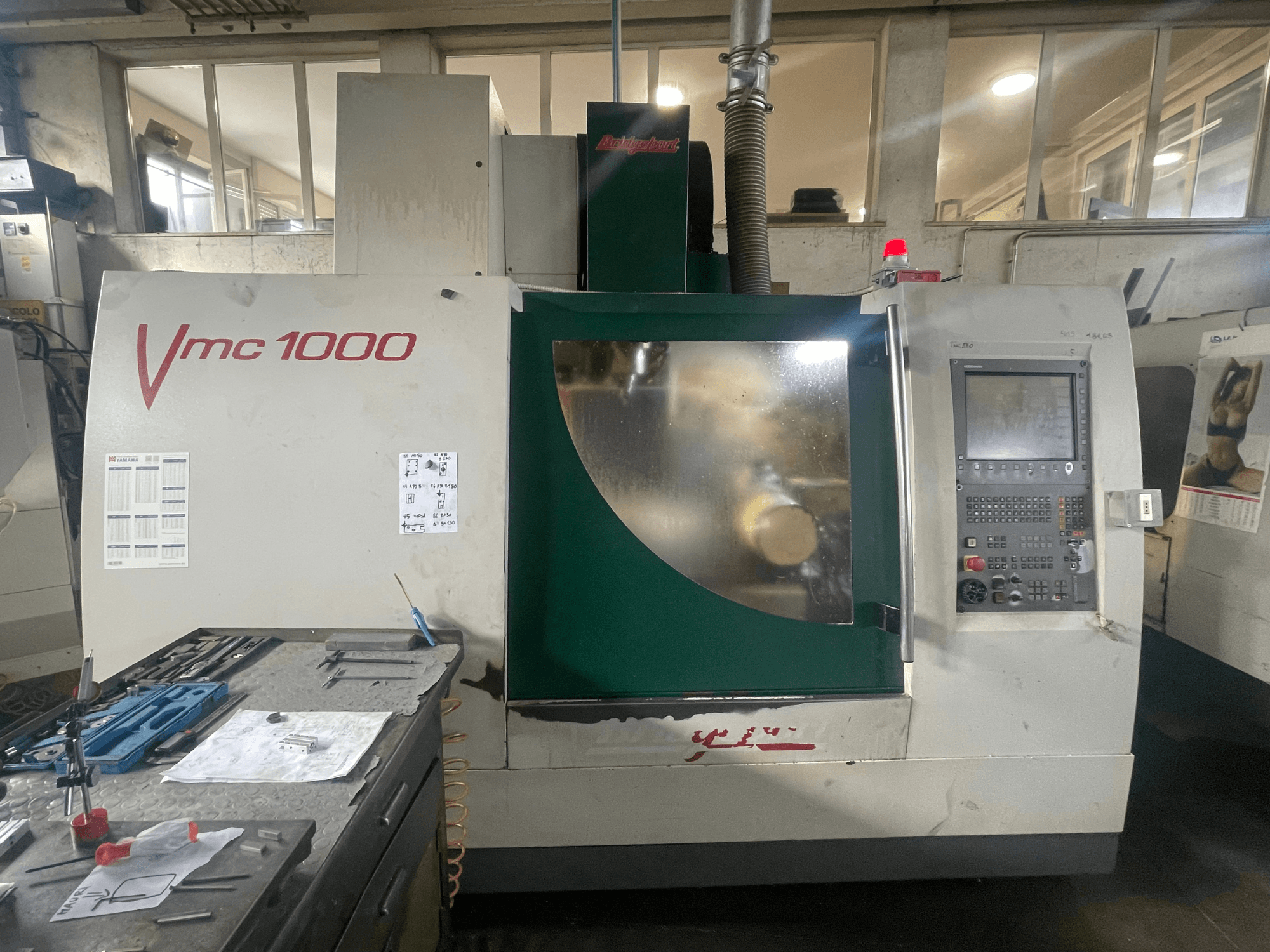 Vertikalusis apdirbimo centras „Bridgeport VMC 1000/30“, vaizdas iš priekio, kuriame matomas valdymo pultas ir pagrindinis korpusas, šalia – įrankiai.