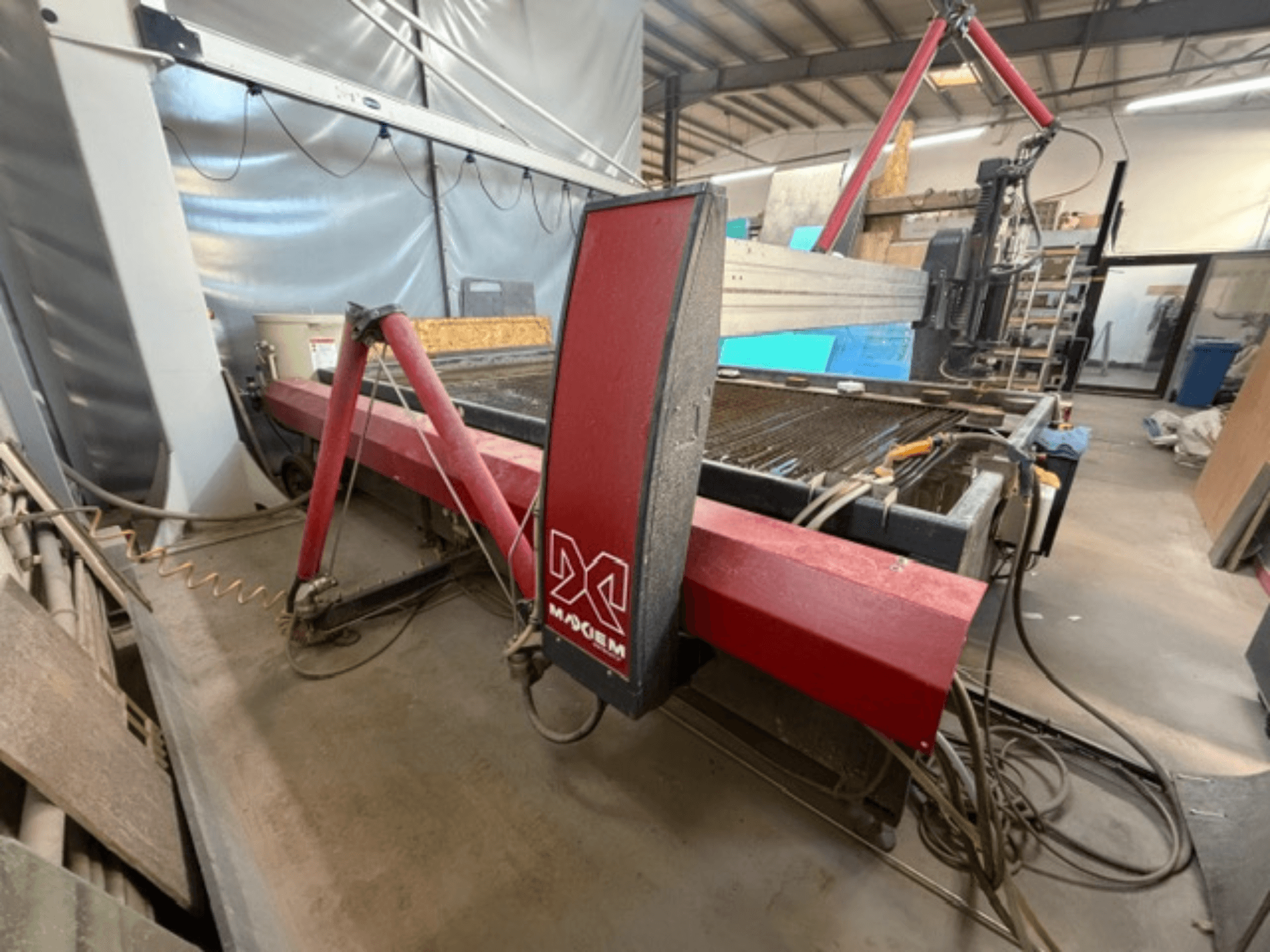 Raudonos spalvos X prekės ženklo pjovimo vandens srove mašina, žiūrint iš šono, matyti mechaniniai komponentai ir vamzdynų detalės.